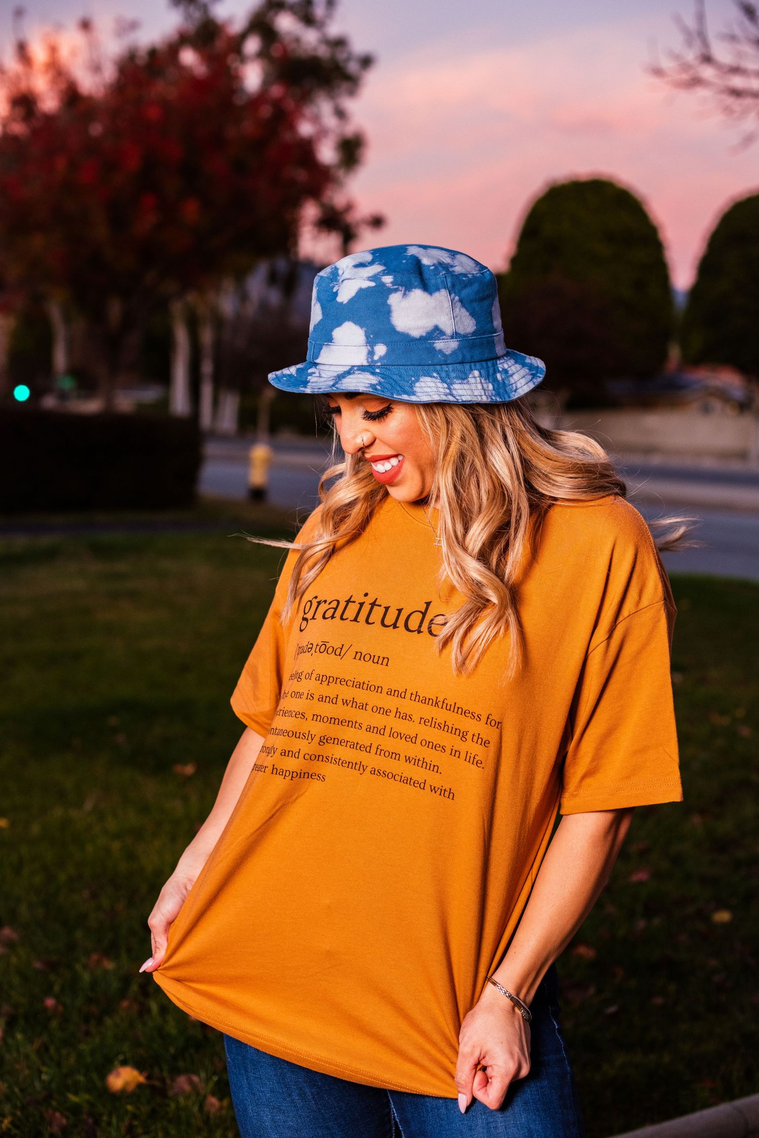 Person wearing cloud-print bucket hat and orange gratitude t-shirt during sunset.