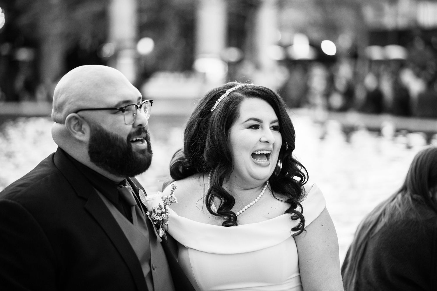 Black and white photo of couple sharing joyful laughter during wedding celebration.