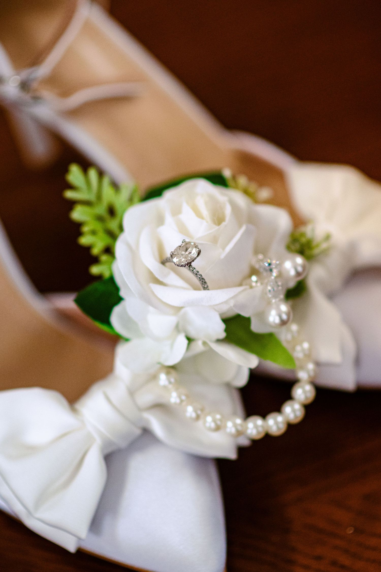 A delicate white floral wedding shoe with pearl and crystal embellishments rests on a dark wooden surface.