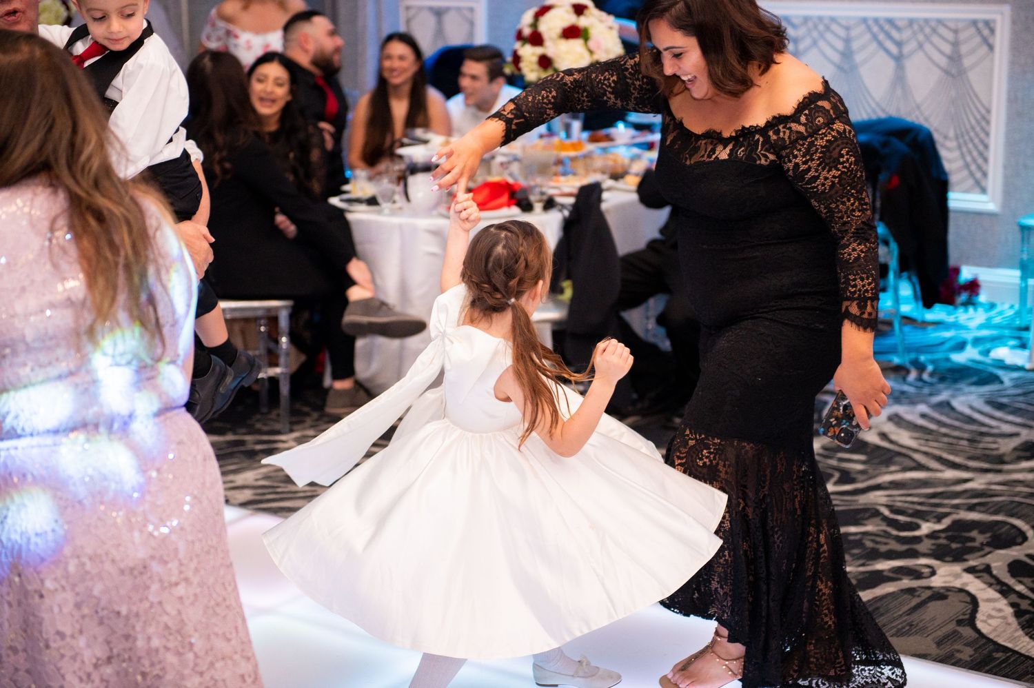 Wedding party members dance and celebrate on a brightly lit dance floor during the reception.
