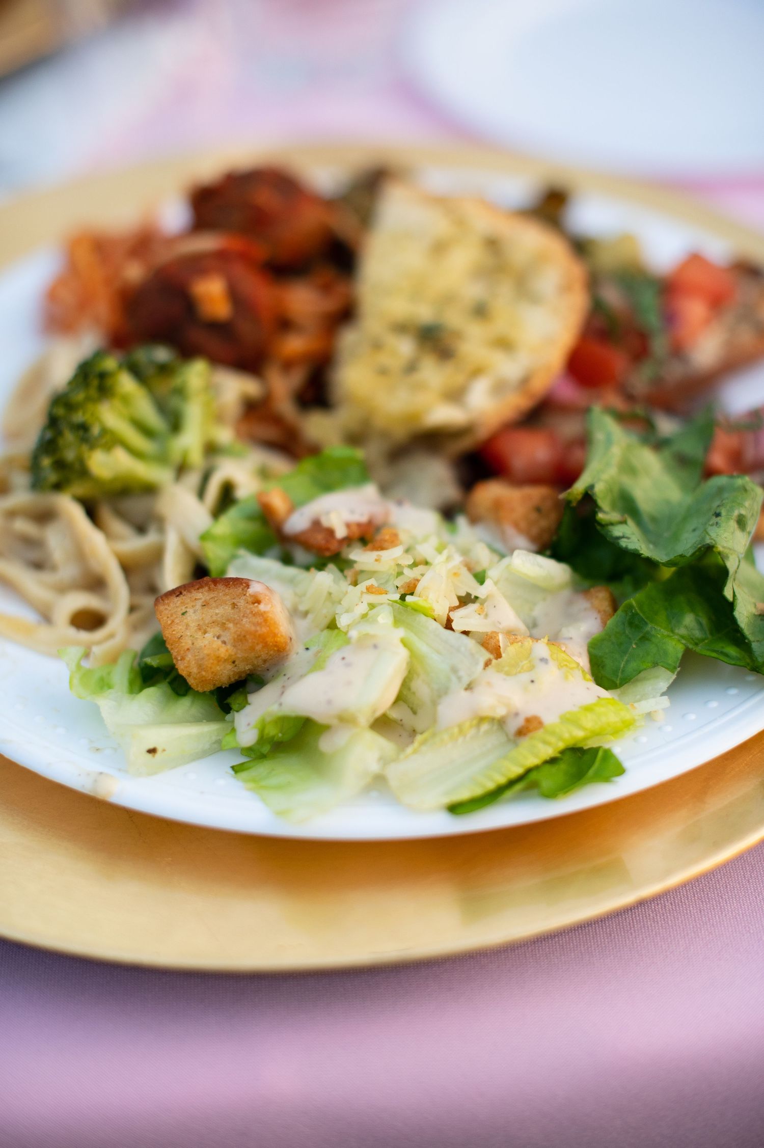 Close-up view of salad plates with fresh vegetables, grilled meats, and pasta served on cream-colored dishes.