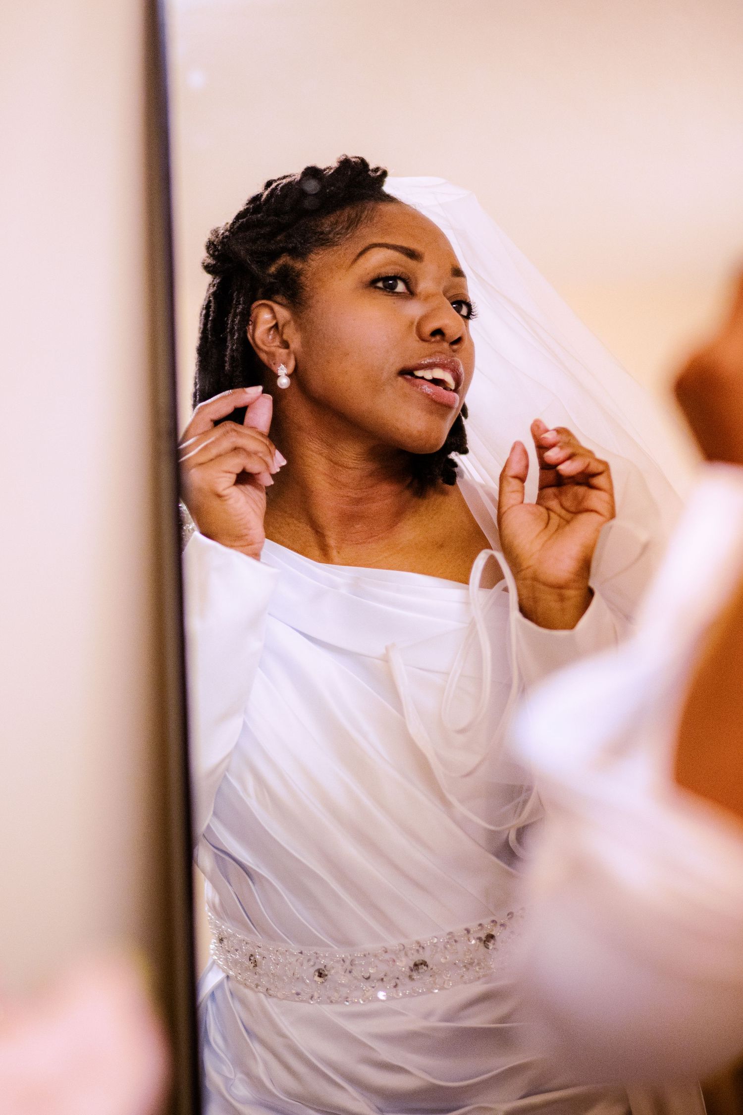 A bride in a white dress and veil poses joyfully during her wedding photoshoot.