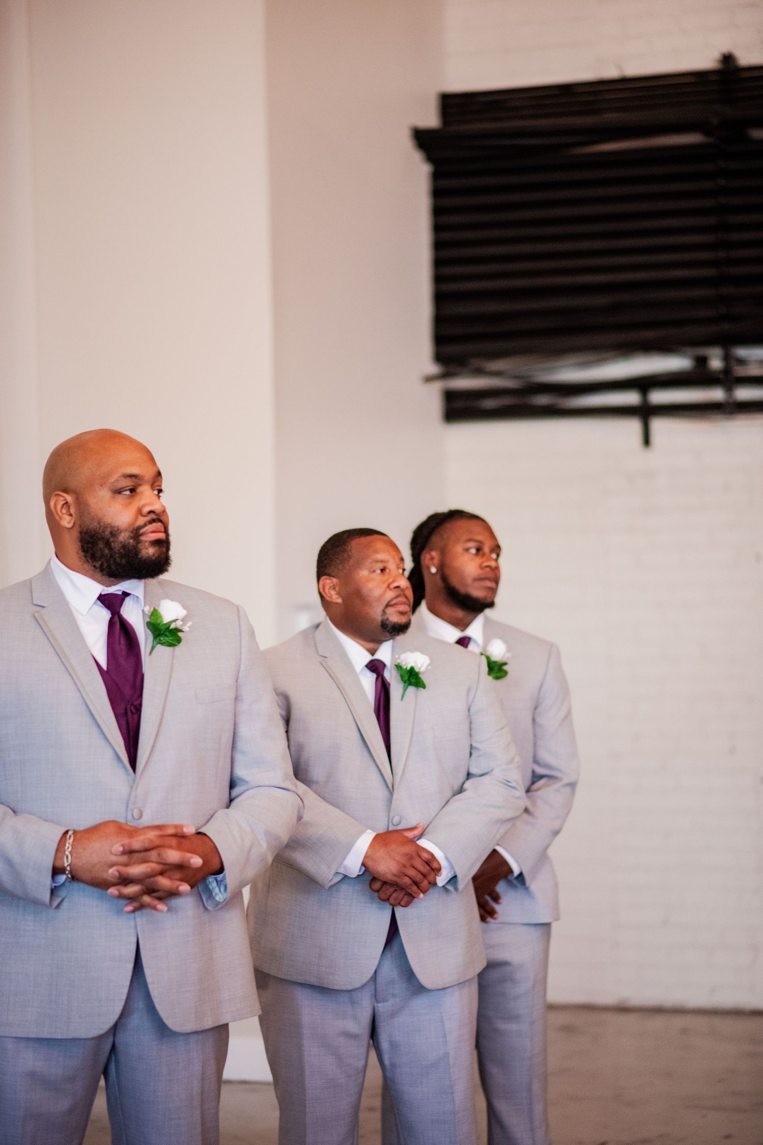 Groomsmen in light grey suits with purple ties and green boutonnieres standing together.