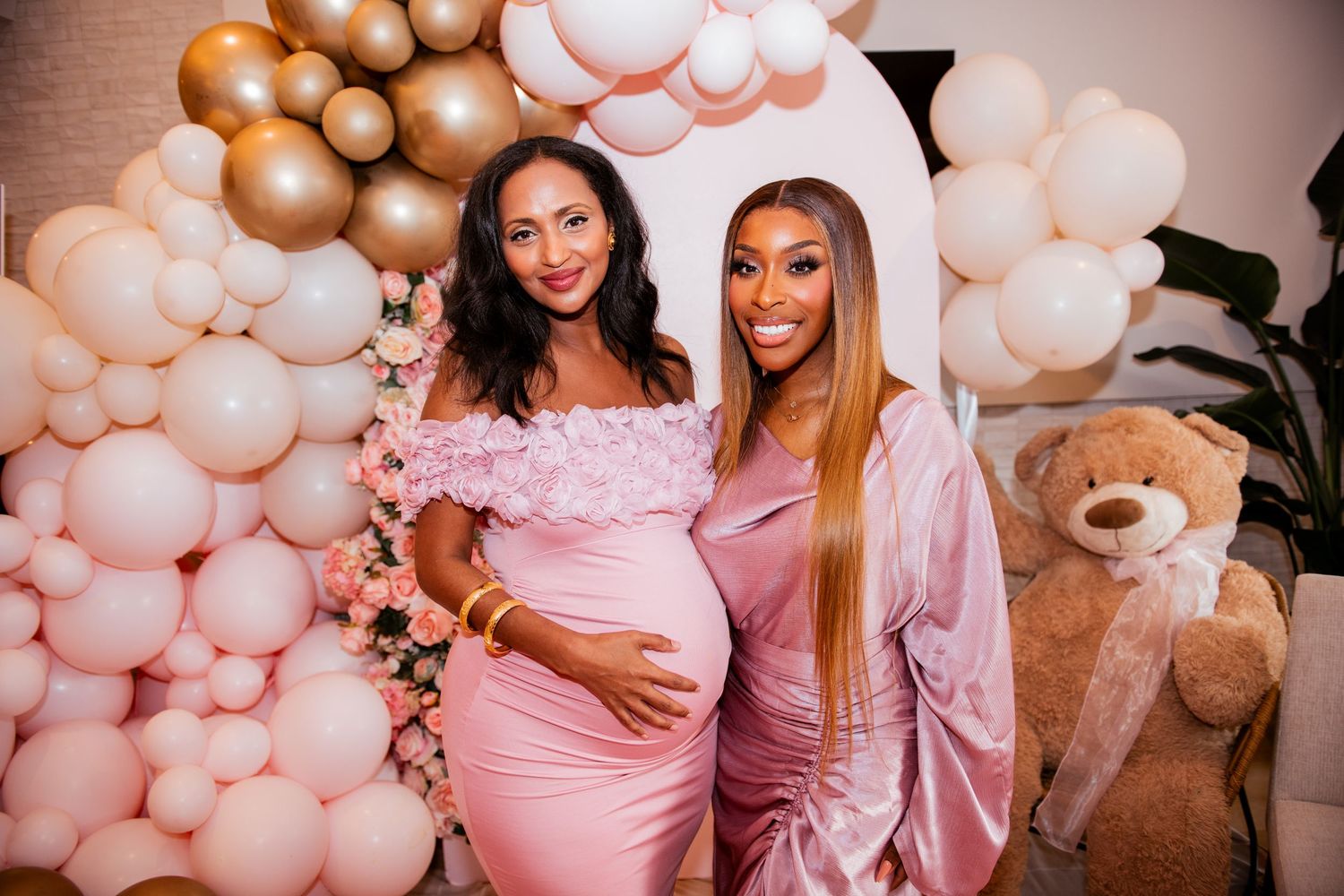 Baby shower celebration with pink and gold balloon decorations and guests wearing pink attire.