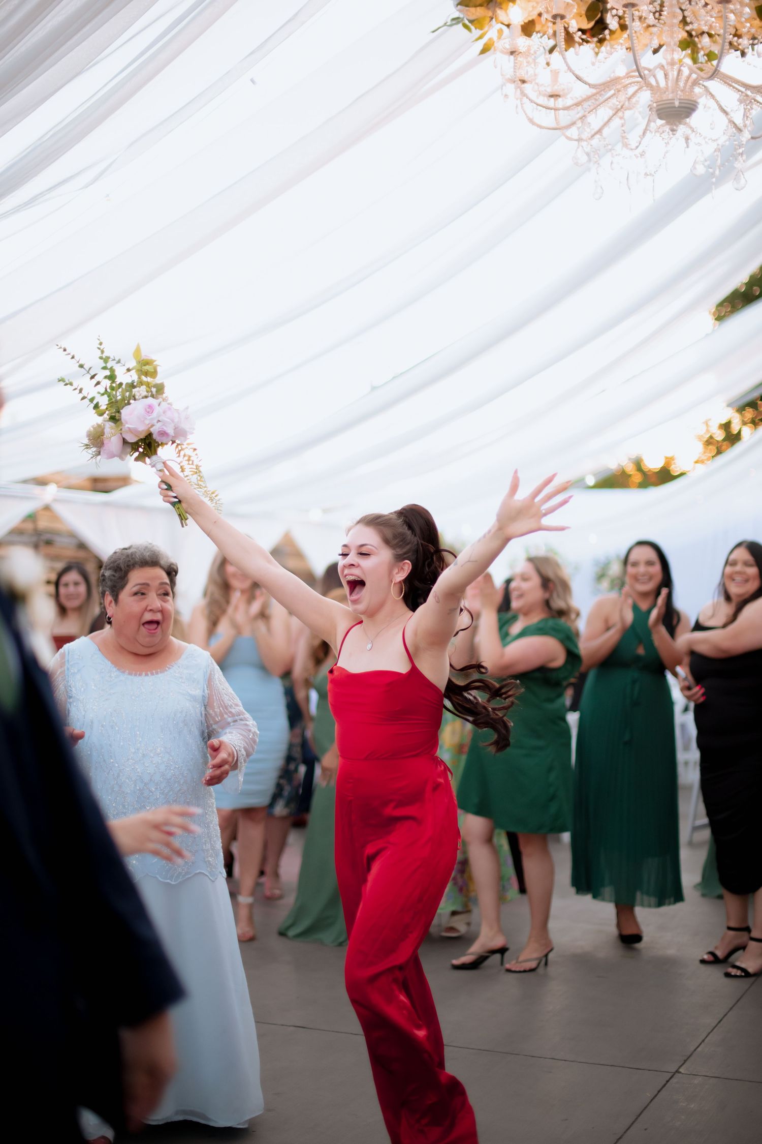 Guests celebrating and dancing at a wedding reception under draped white tent with chandelier.