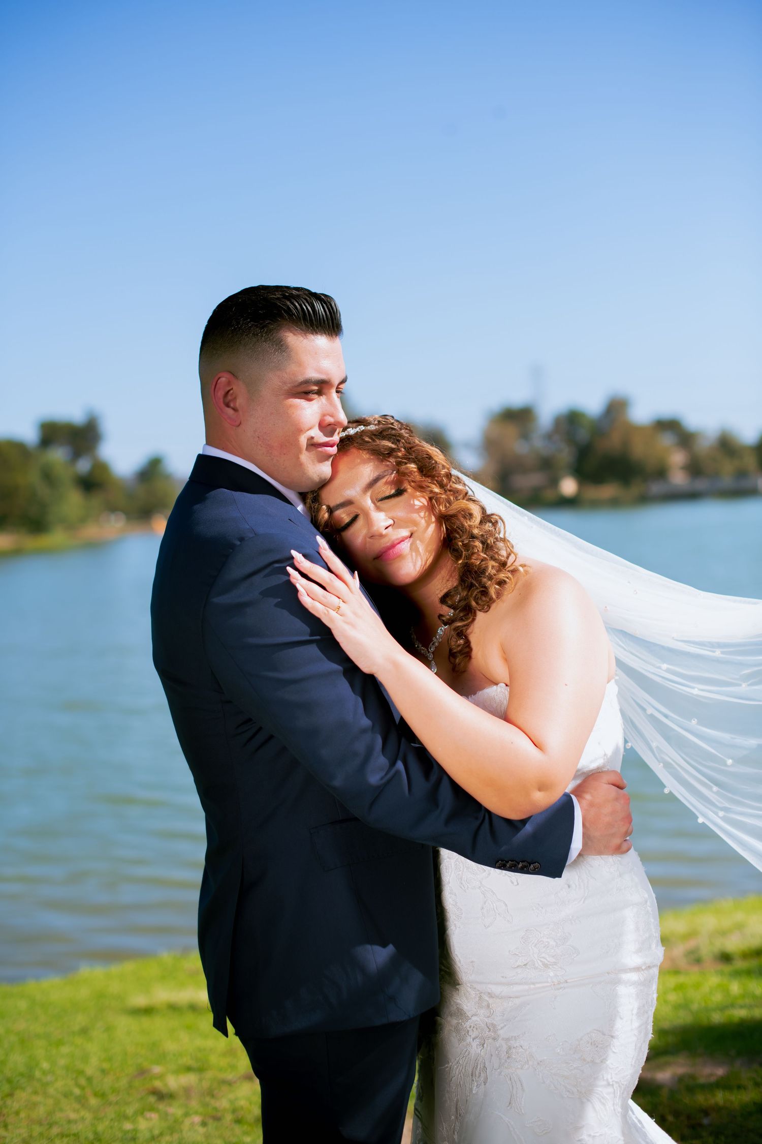 Intimate moment captured between newlyweds on grassy shore with Legg lake in background.