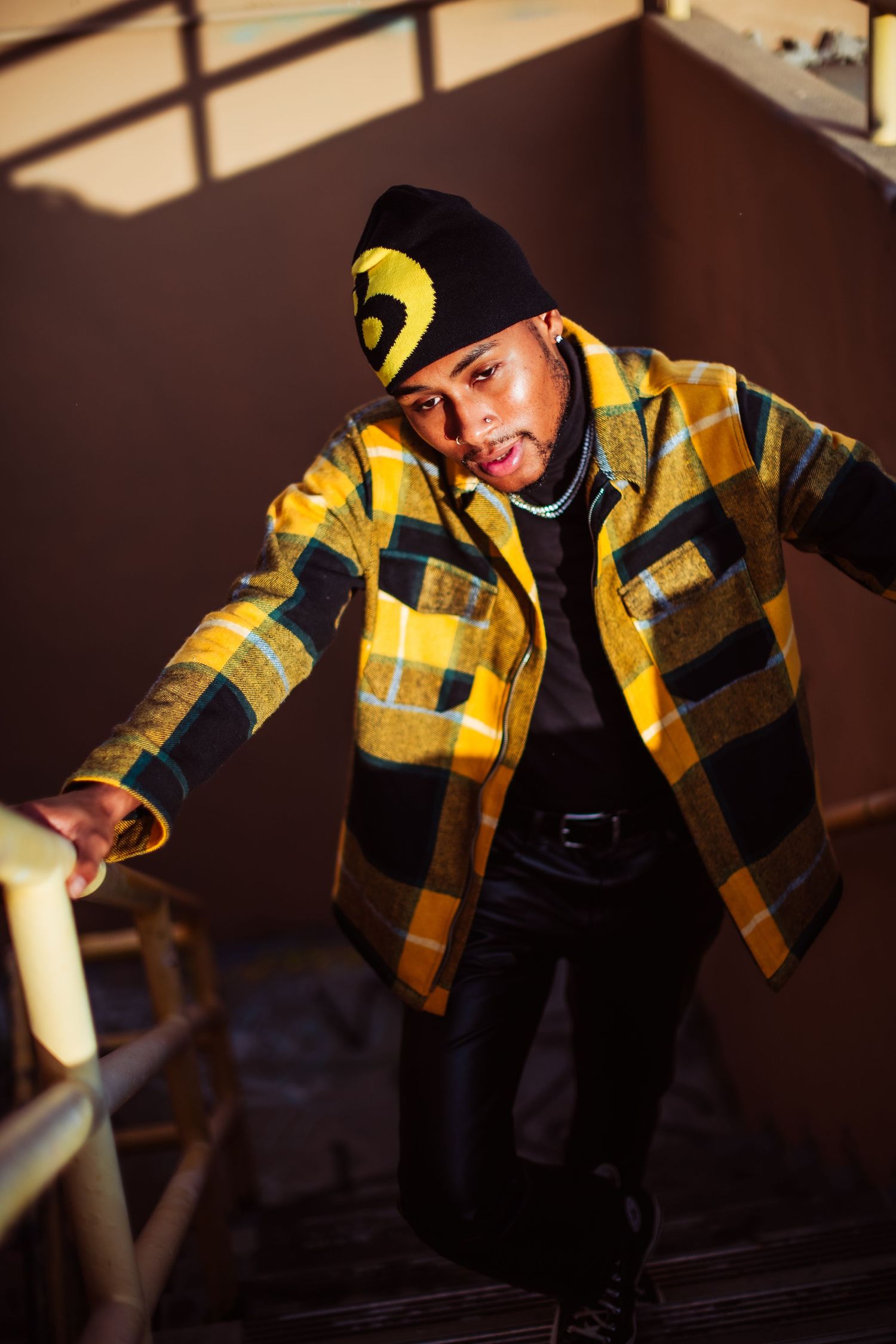 A dancer in a yellow plaid jacket performs a breakdancing move against a dark background.