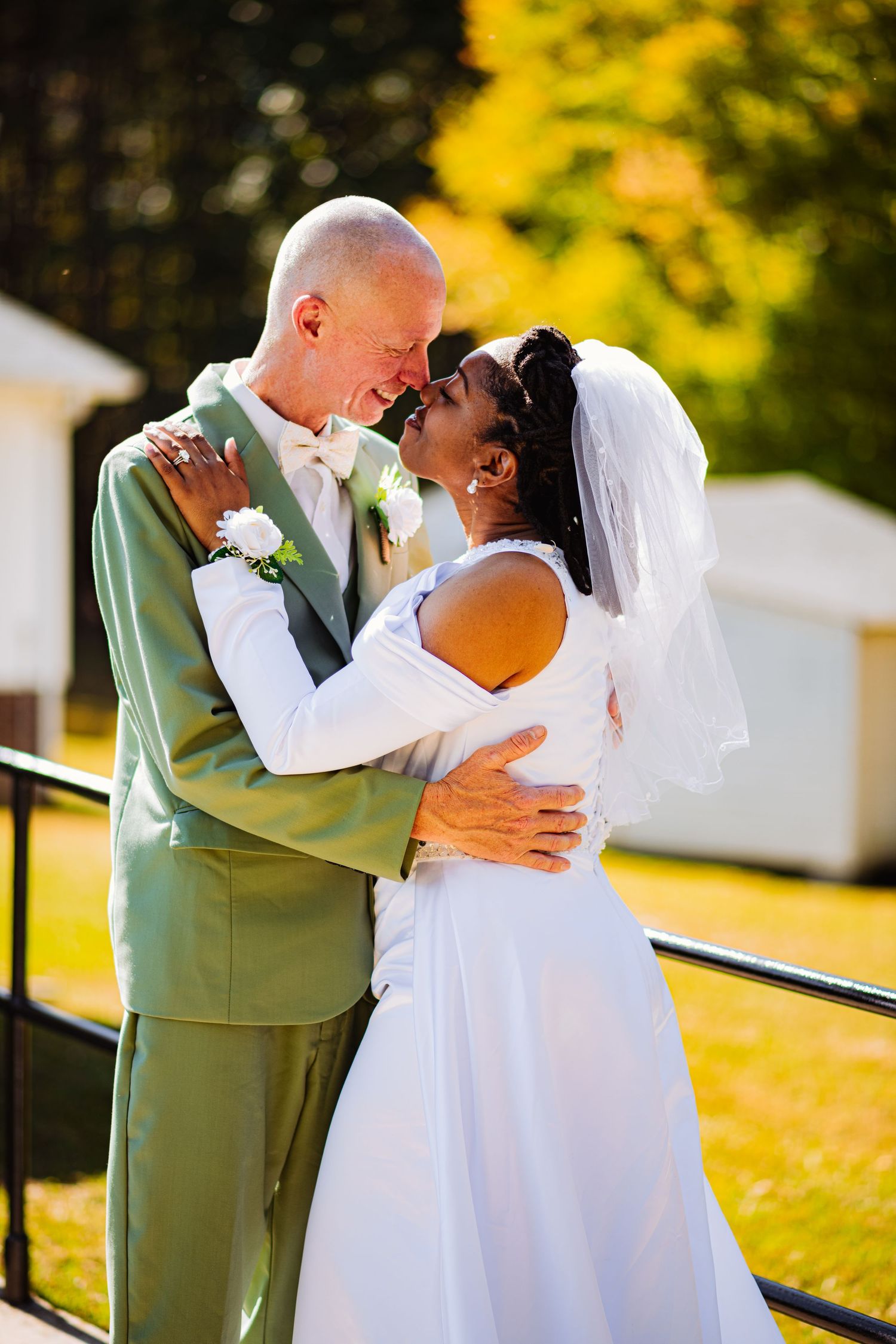 A couple shares a romantic kiss outdoors in formal wedding attire on their special day.