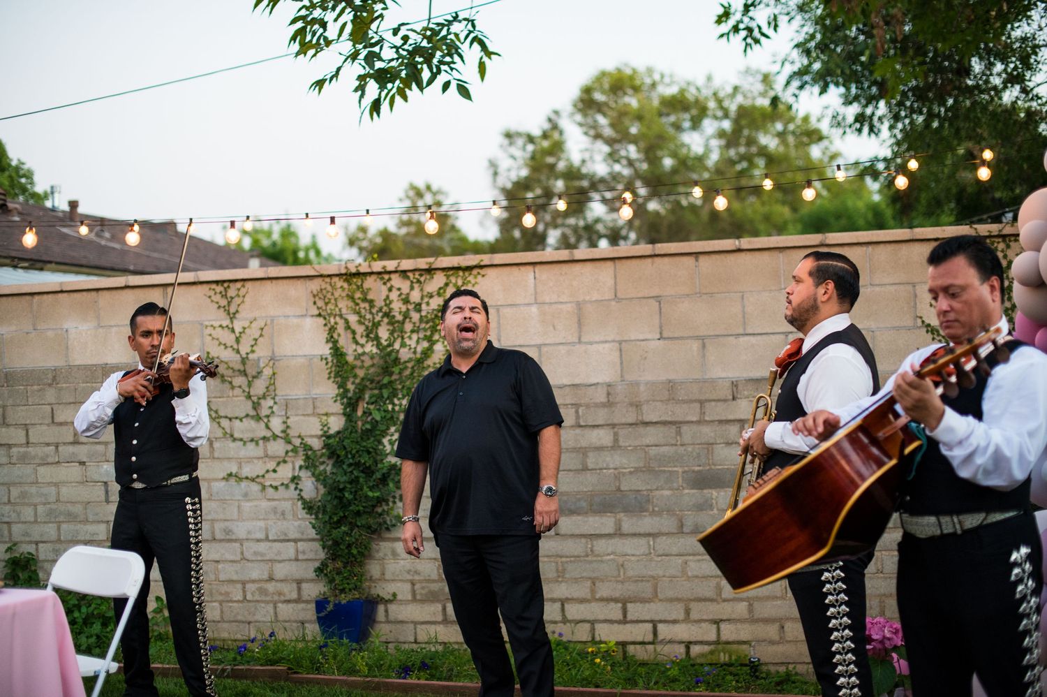 Musicians performing with string instruments at an outdoor evening event with string lights overhead.