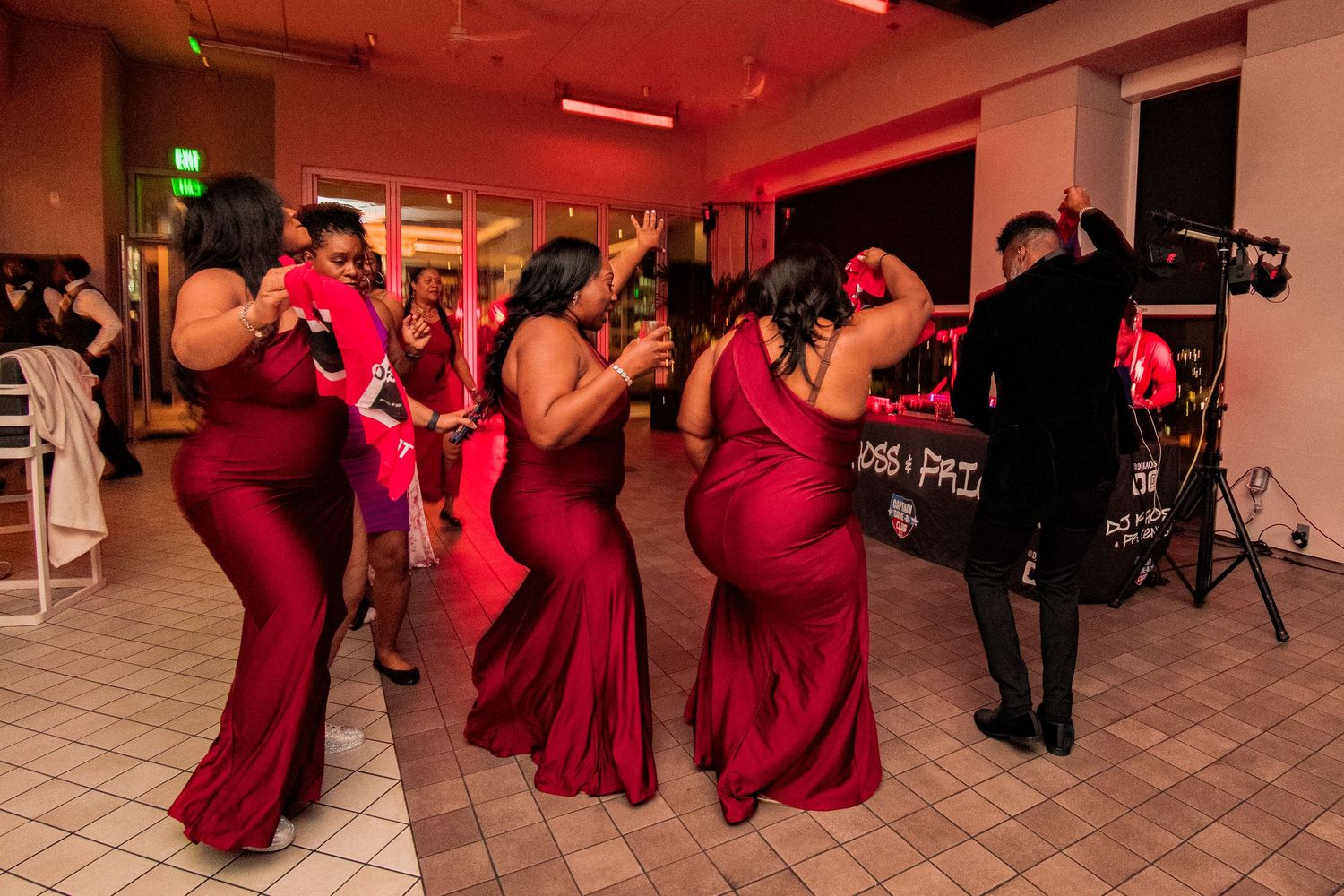 Wedding reception dance floor illuminated with red lighting and guests dancing in burgundy attire.