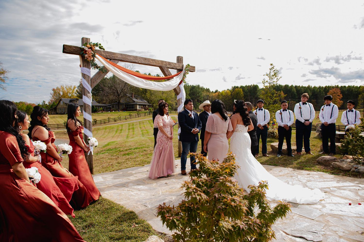 Wedding ceremony taking place outdoors with wooden cross and floral arrangements on display.