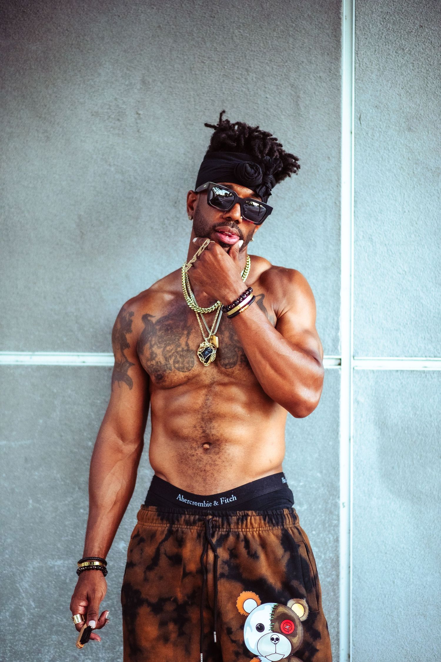 LongLiveCzar posing shirtless against a light background wearing sunglasses and printed shorts with a teddy bear design Breaking Beariers.
