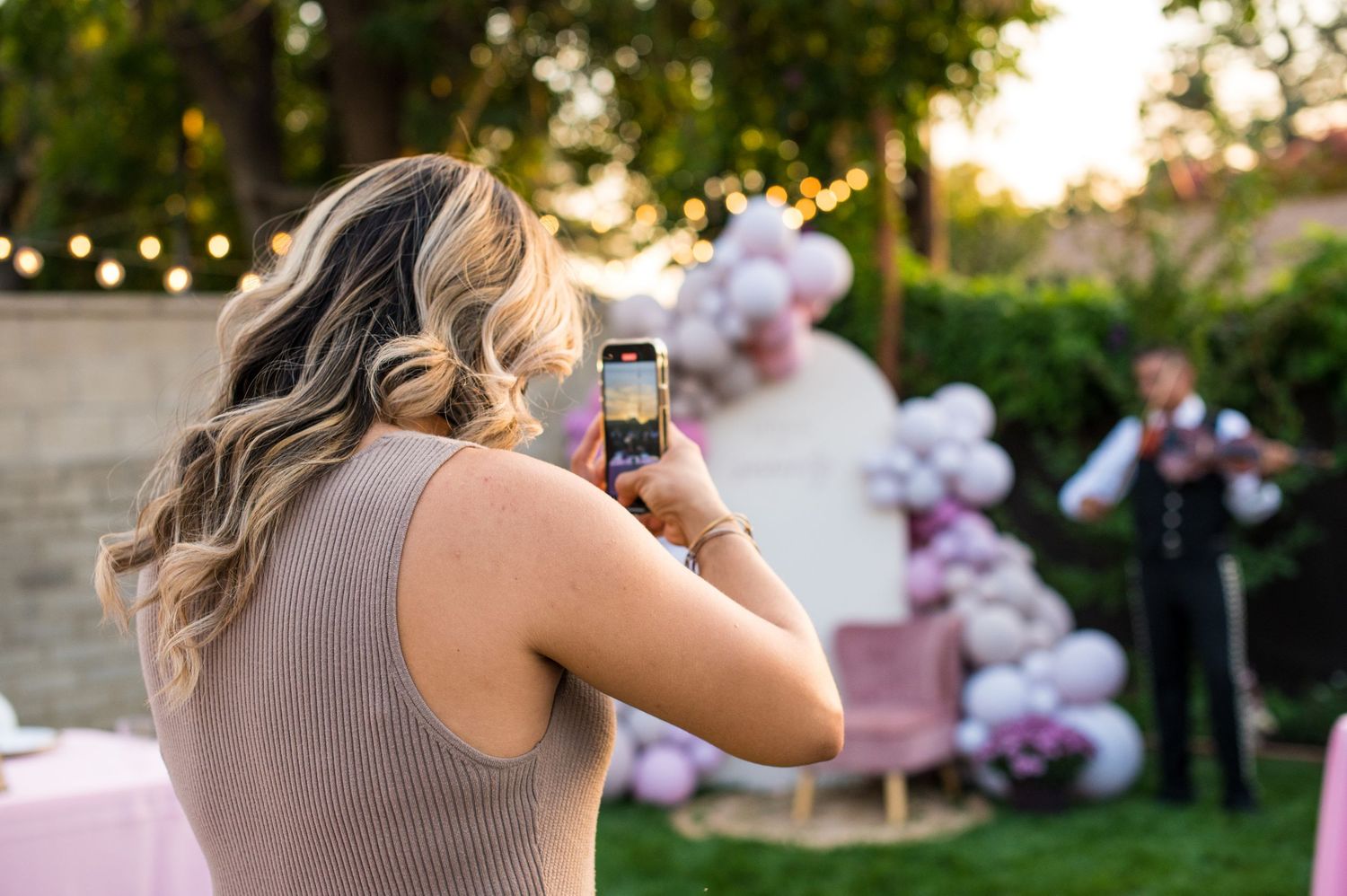 Guests at an outdoor wedding reception toast with champagne glasses during golden hour sunset.