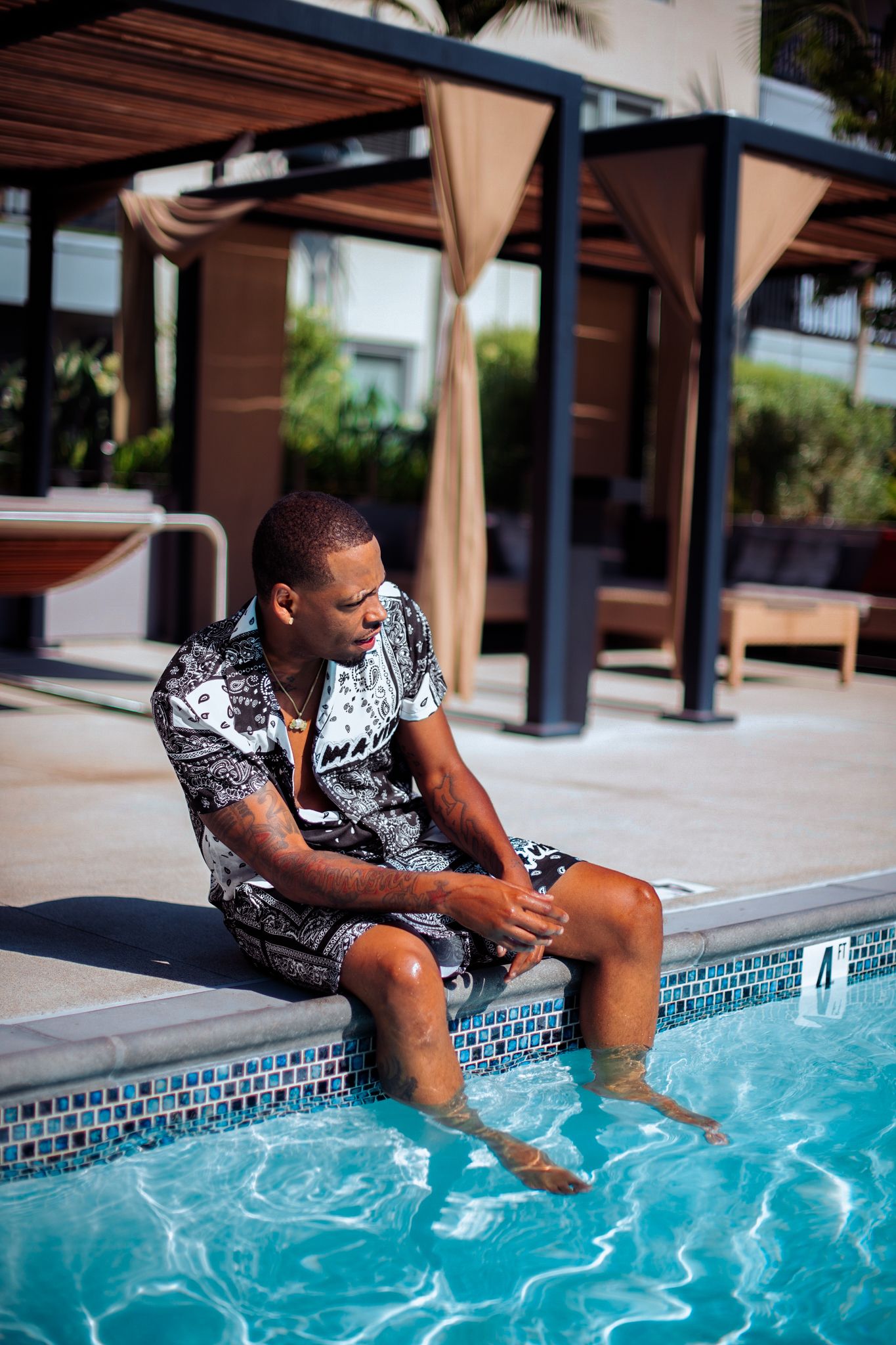 Person in patterned outfit sits at pool edge dipping feet in blue water.