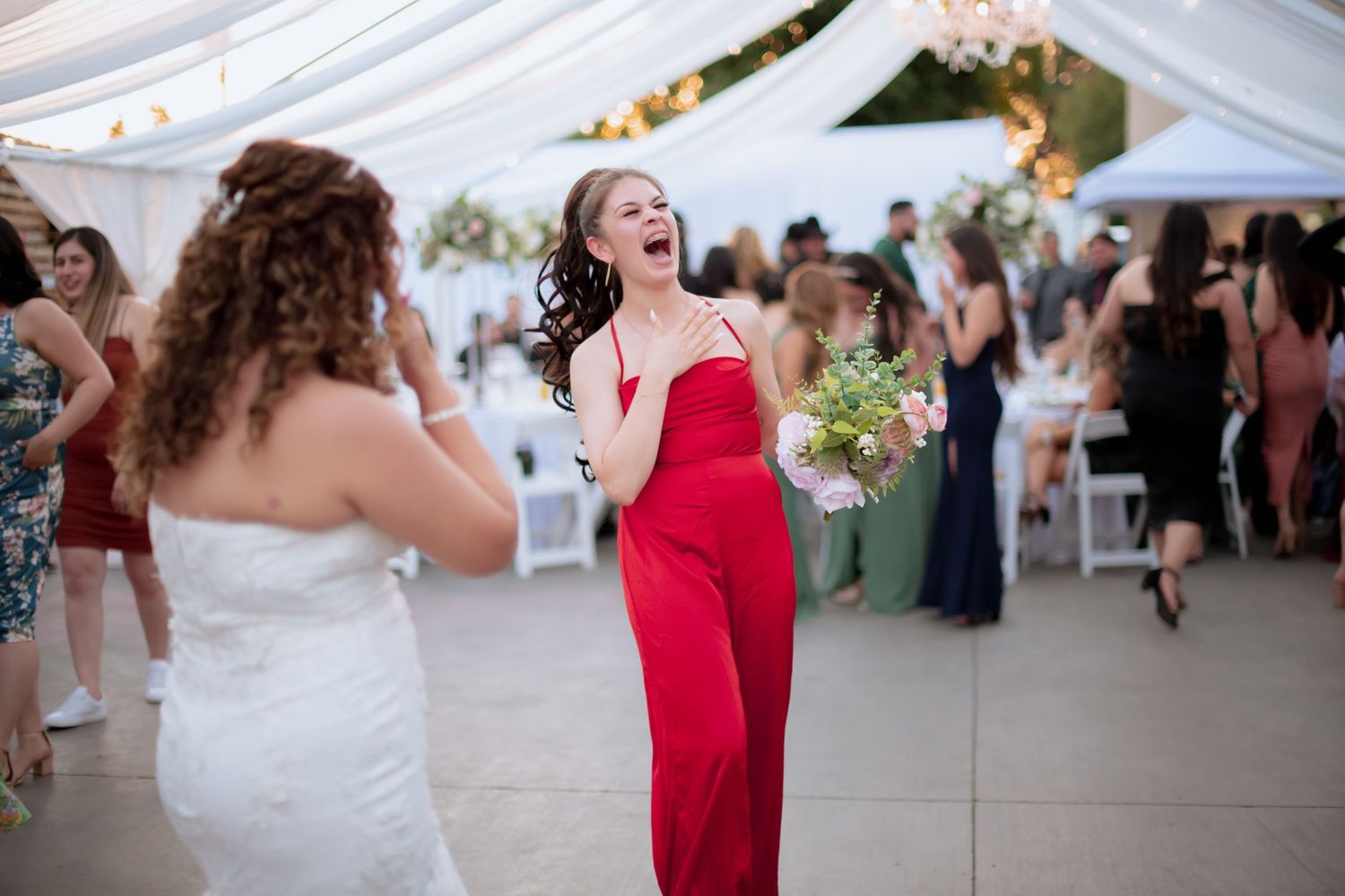 Wedding party dancing energetically under white tent during reception celebration.