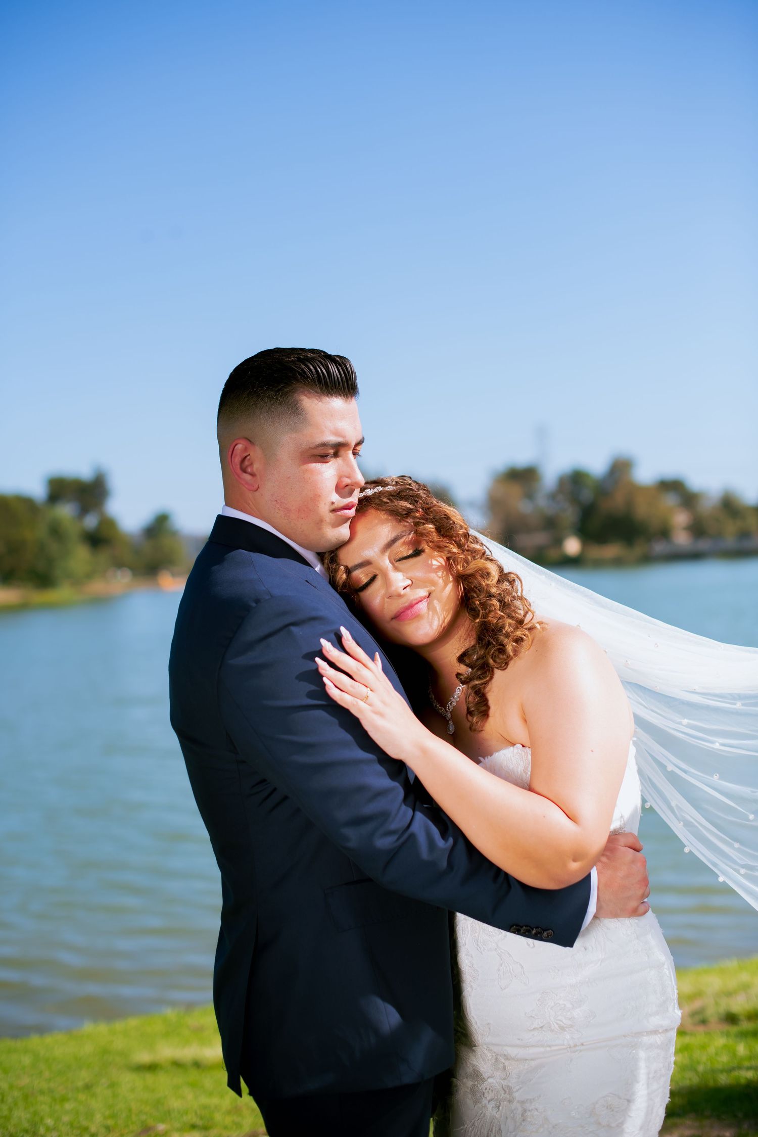 Tender embrace between newlyweds on a sunny day by the waterfront.
