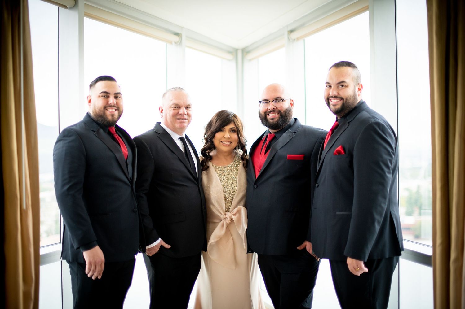 A group of people wearing formal black attire pose together in a bright room with windows and curtains.