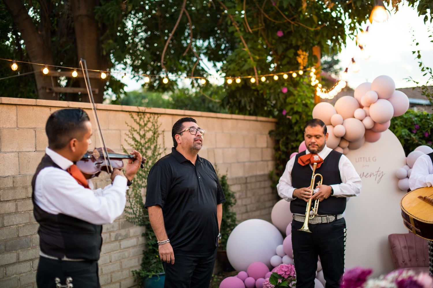 Festive outdoor gathering with pink and white balloon arrangements and string instruments being played at dusk.
