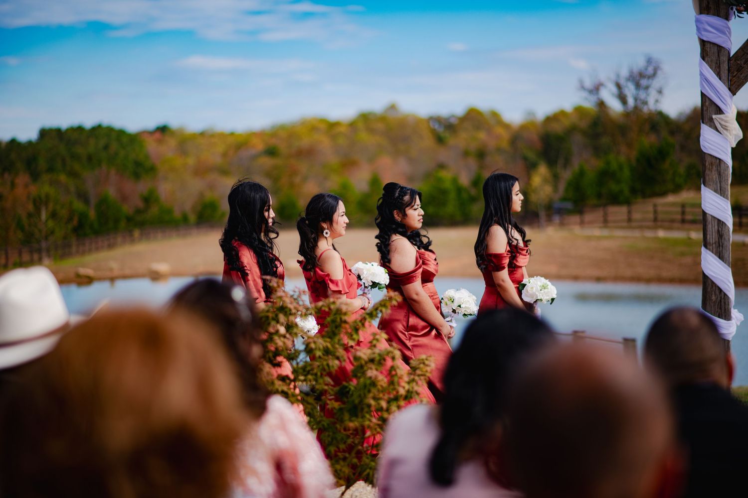 Wedding party poses together outdoors with beautiful lake and blue sky in the background.
