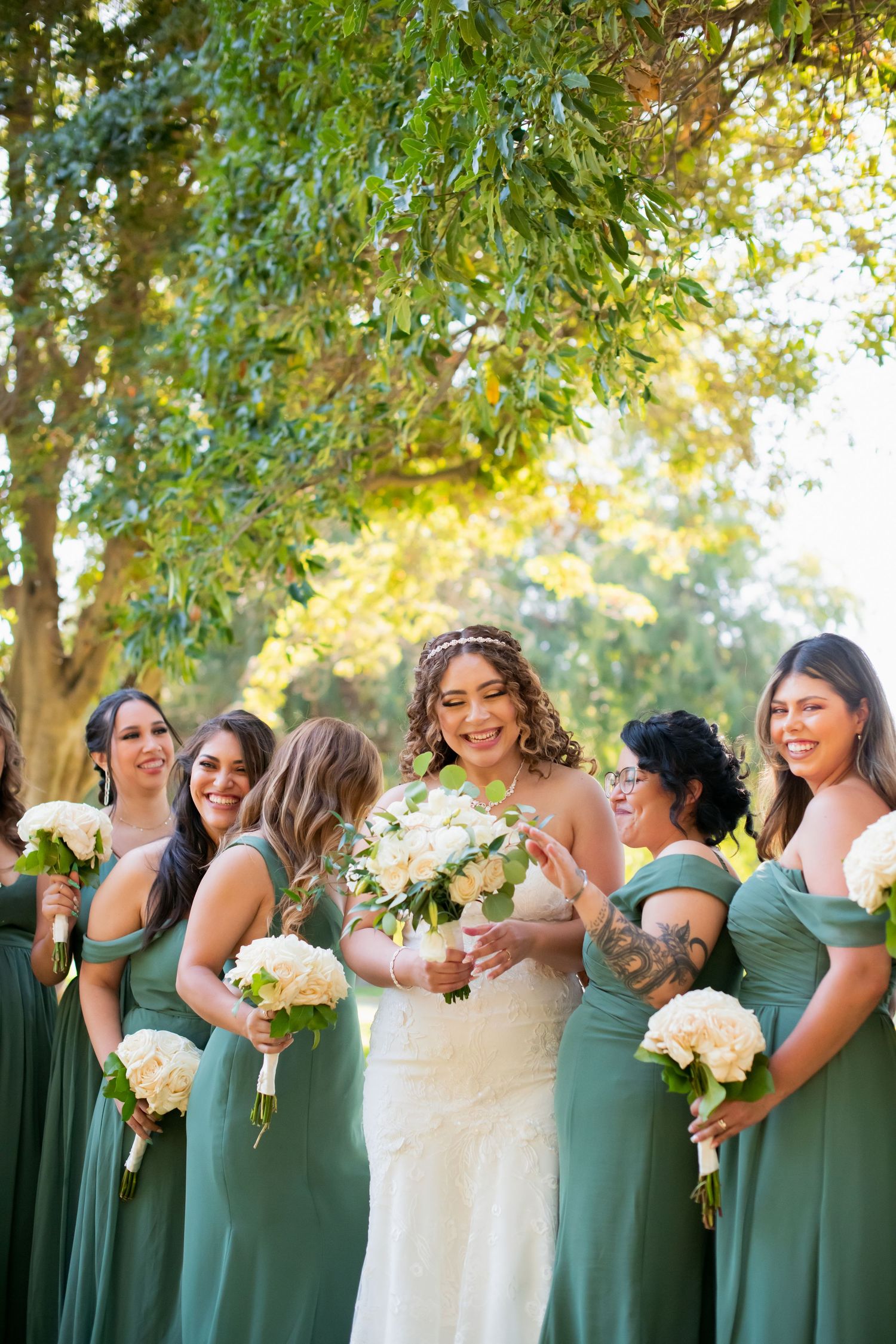 Wedding party members share candid laughs during outdoor photo session in matching sage dresses.