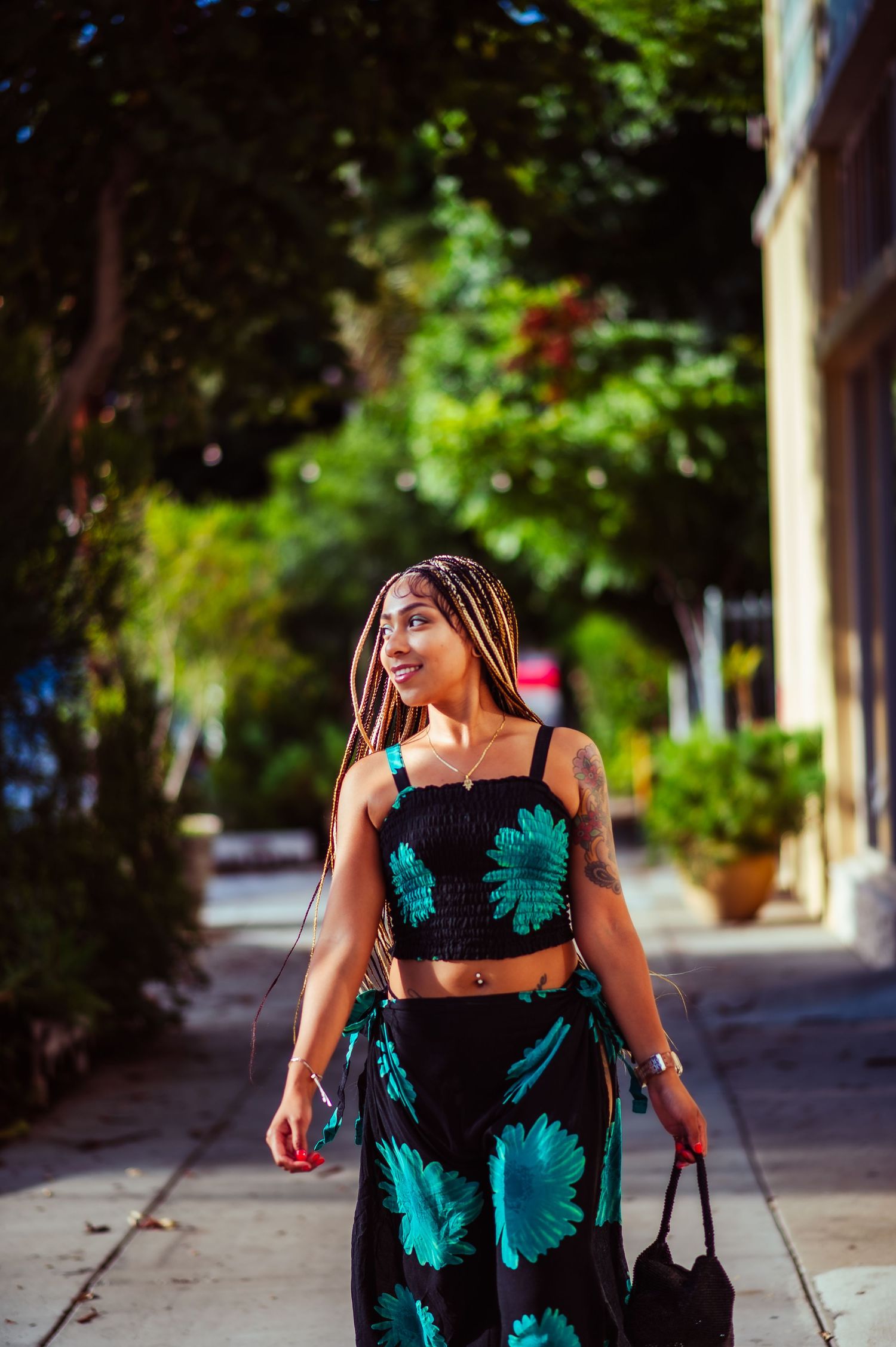 A summer fashion photoshoot featuring a black and teal floral dress on a sunny sidewalk.