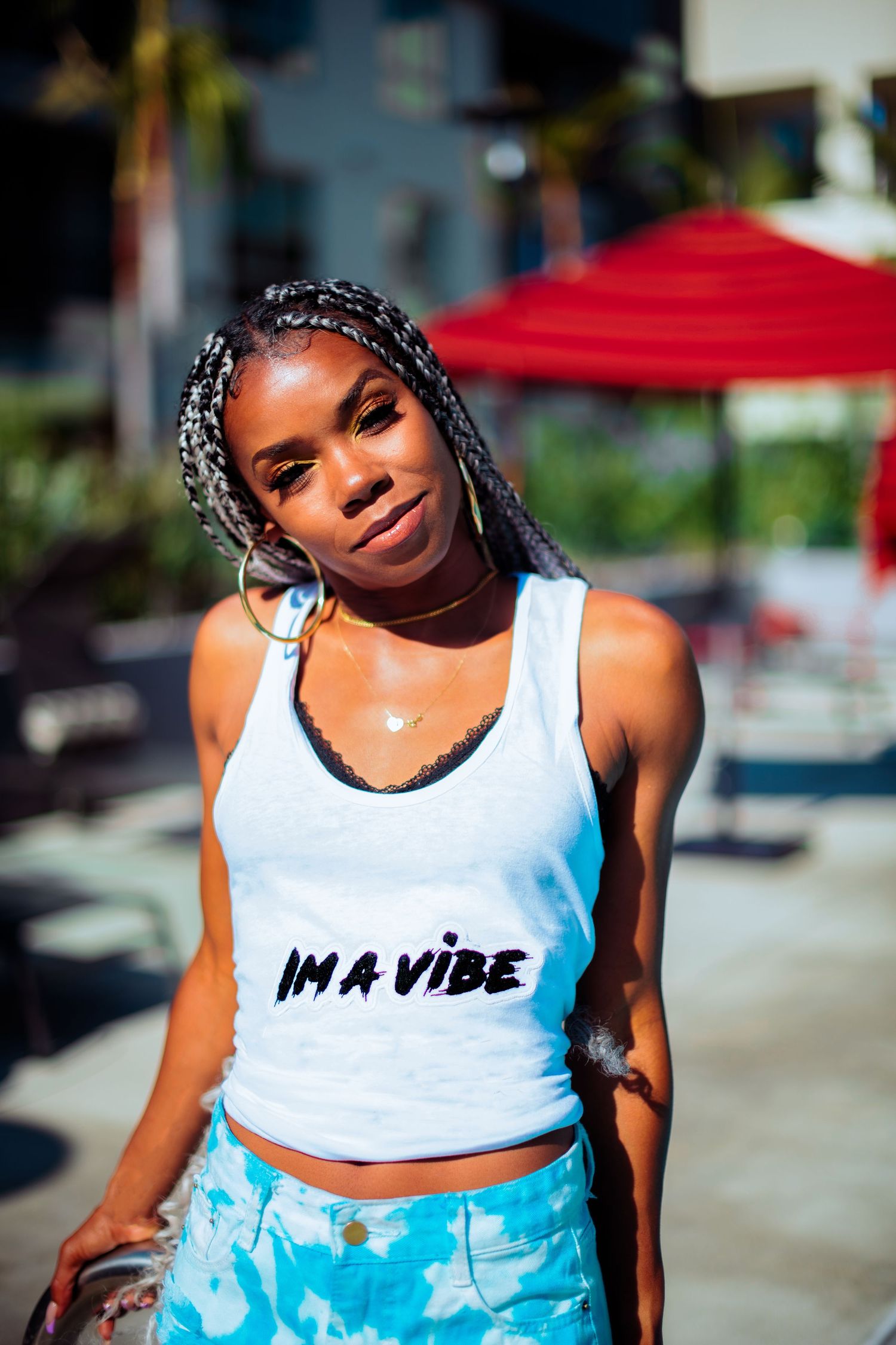 A person in a white crop top and blue patterned pants poses outdoors in bright sunlight.