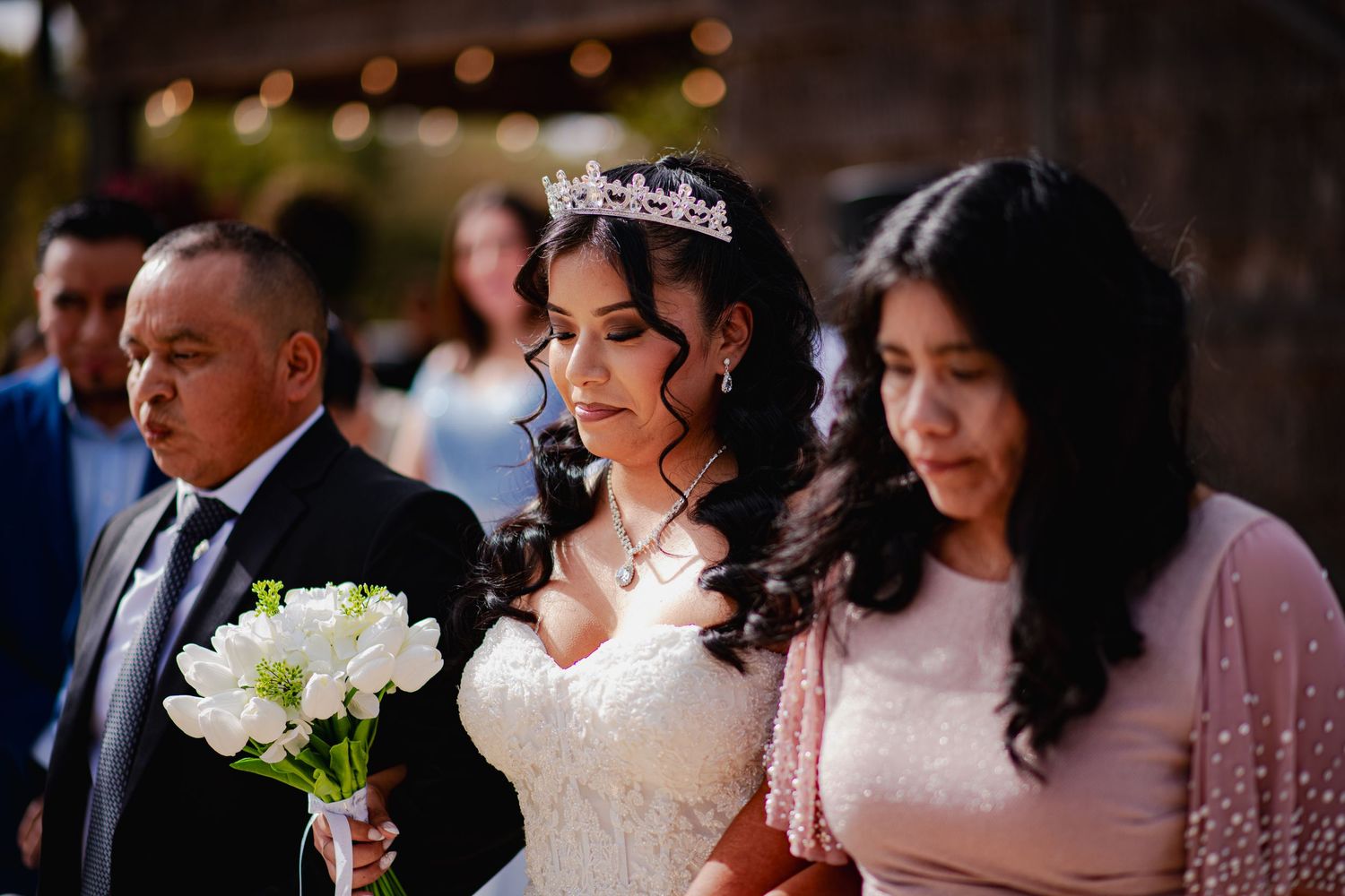 Wedding party members stand together during an elegant evening ceremony with decorative lighting and floral arrangements.