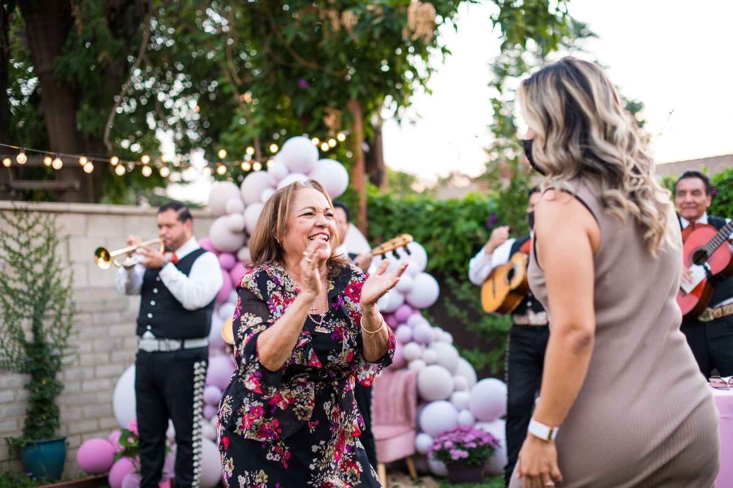 Wedding guests share joyful moments during an outdoor celebration with string lights and greenery in the background.