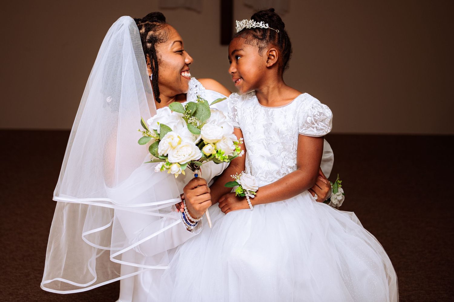Two people in wedding attire share an intimate moment while holding white bouquets.