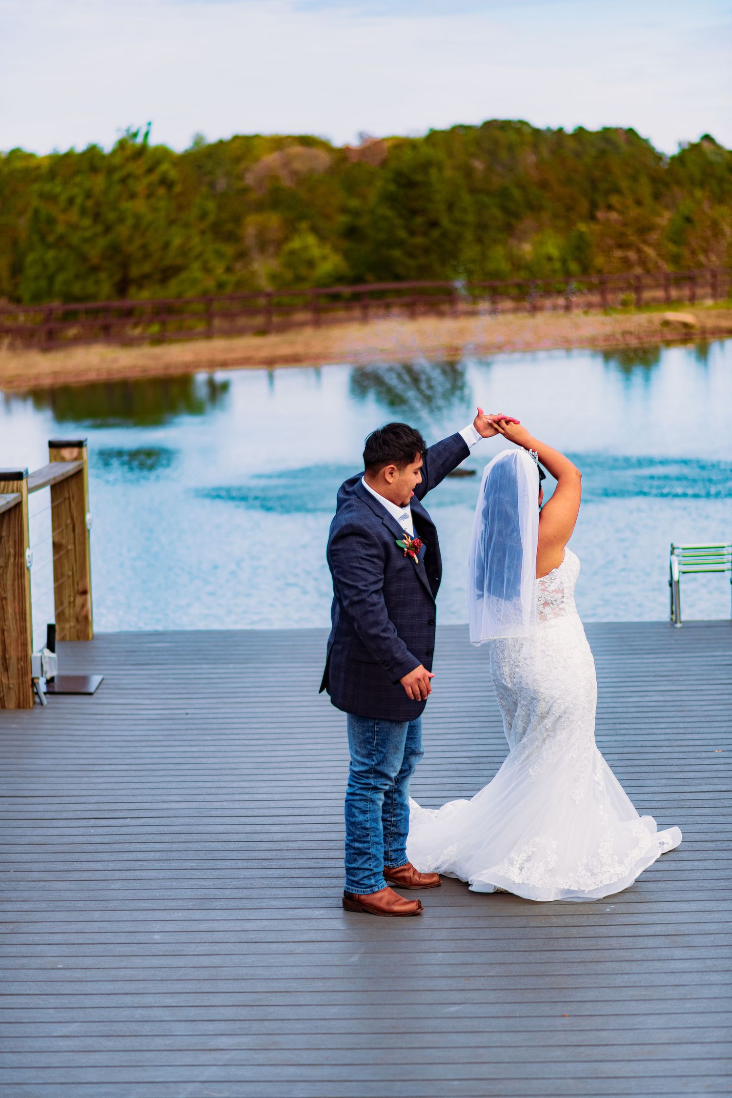 A couple shares a romantic moment on a wooden deck overlooking a serene lake during their wedding celebration.