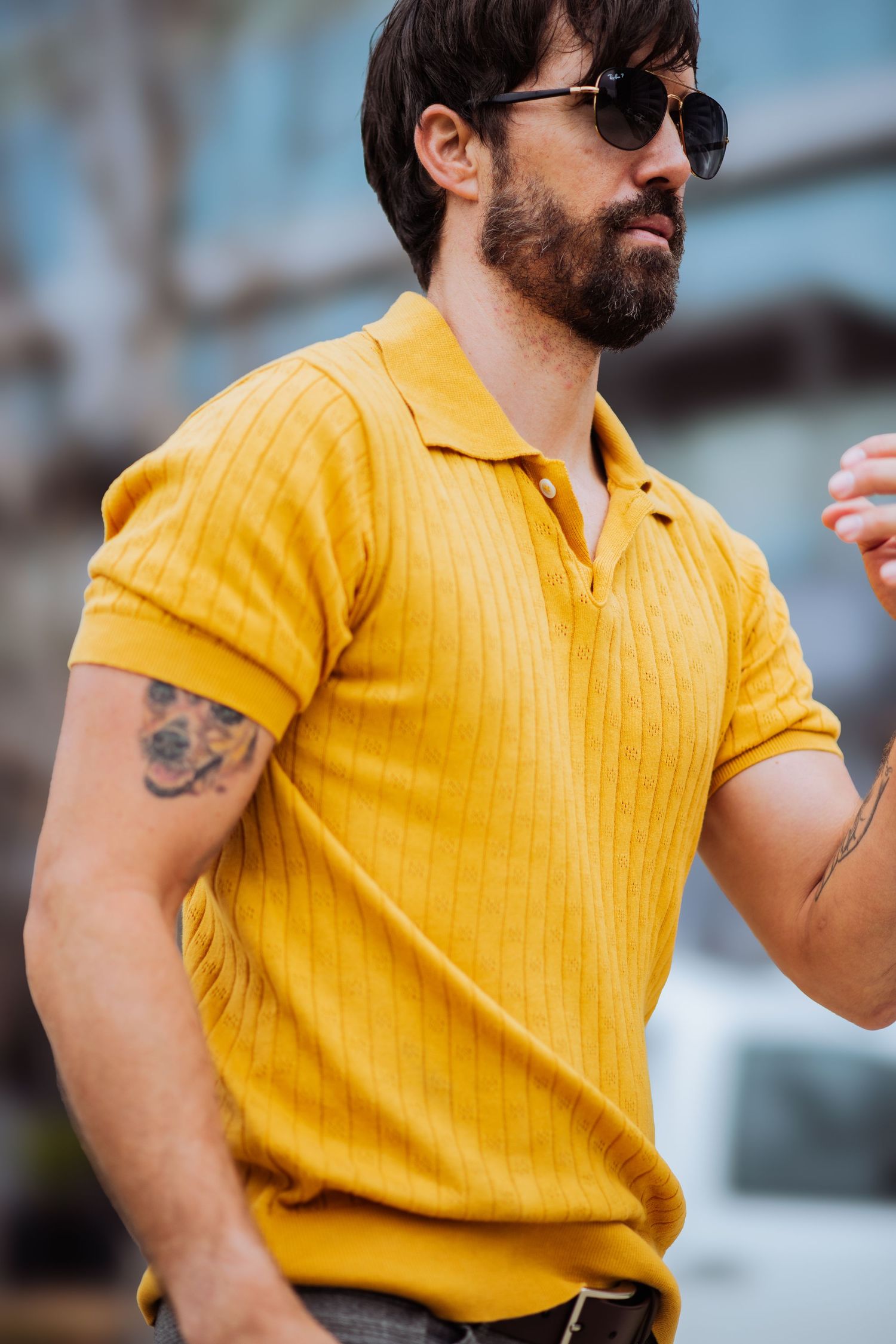 Dynamic pose of person in bright yellow polo showing movement against urban backdrop.