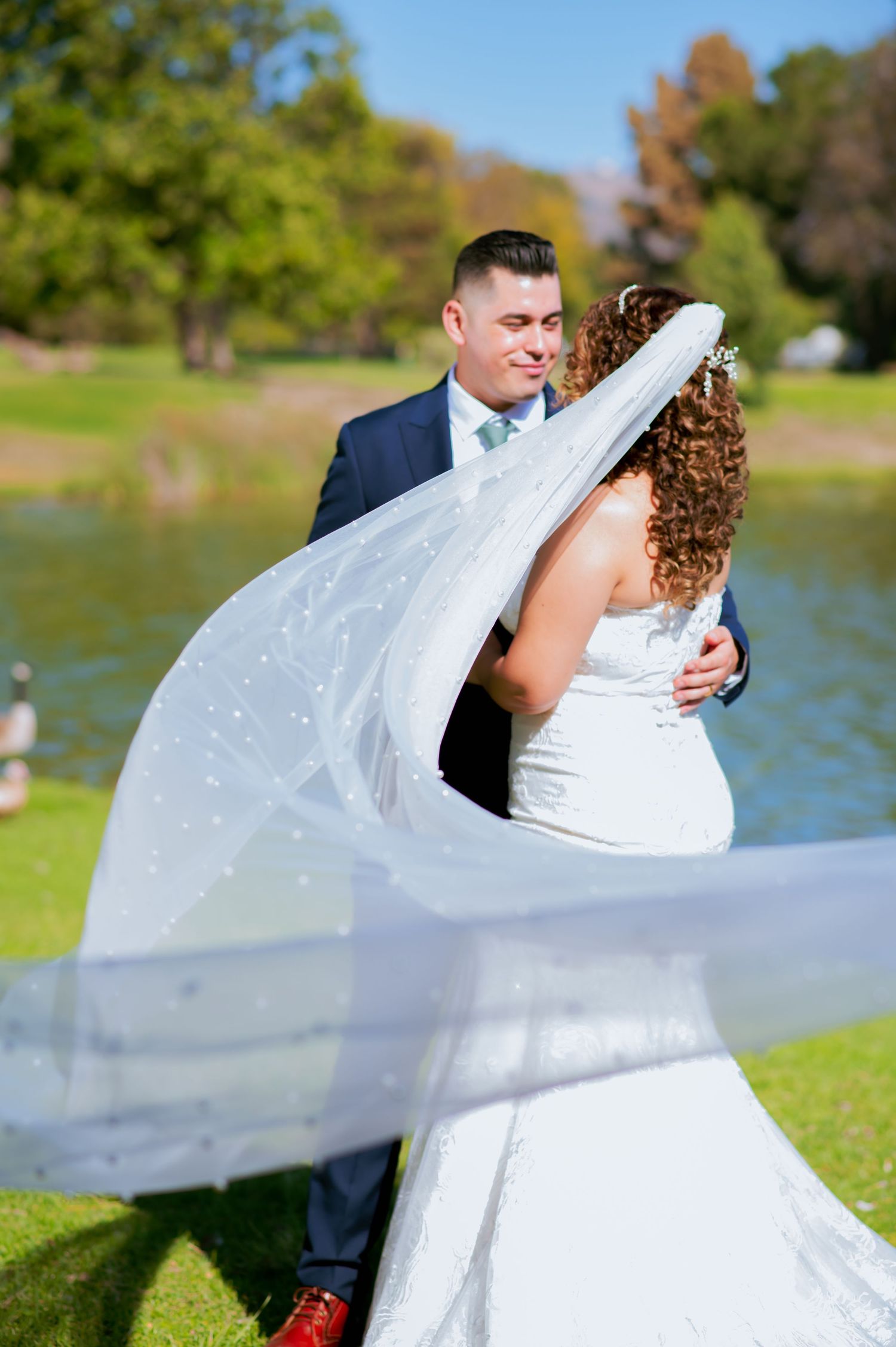 Romantic wedding sequence with billowing white veil catching breeze by lakeside.