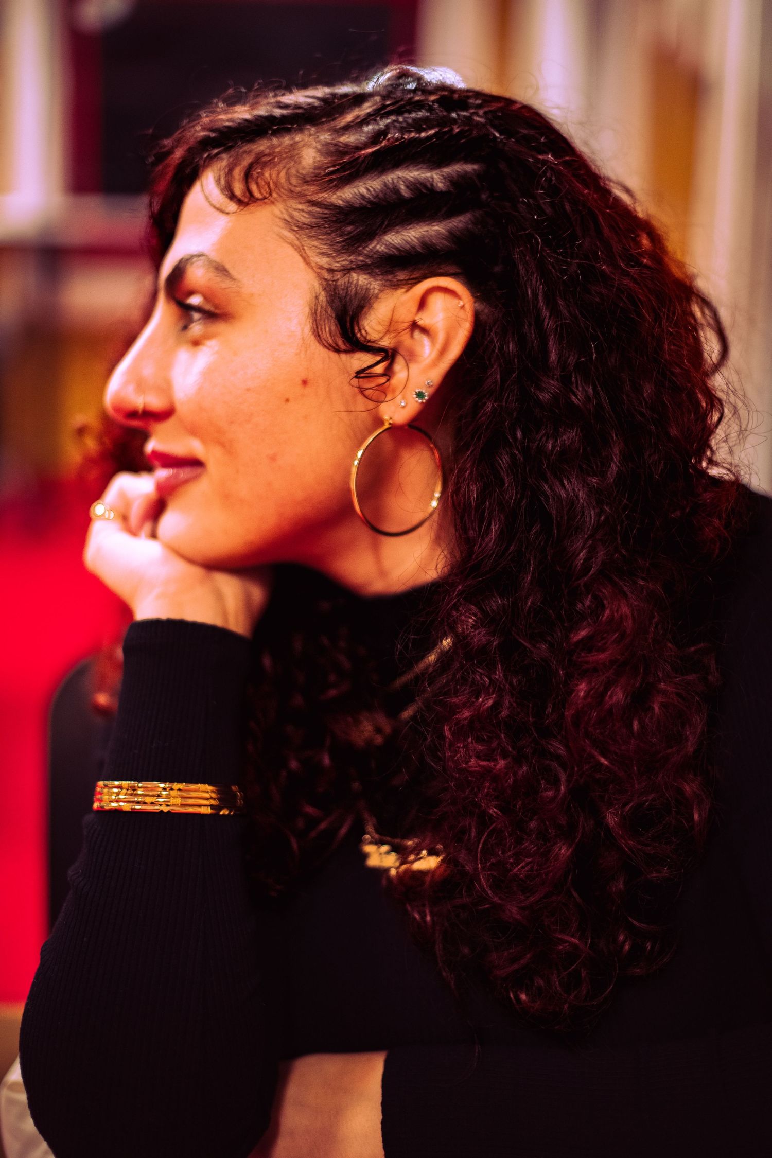 Profile view of person with curly dark hair against warm-toned lighting and red background.