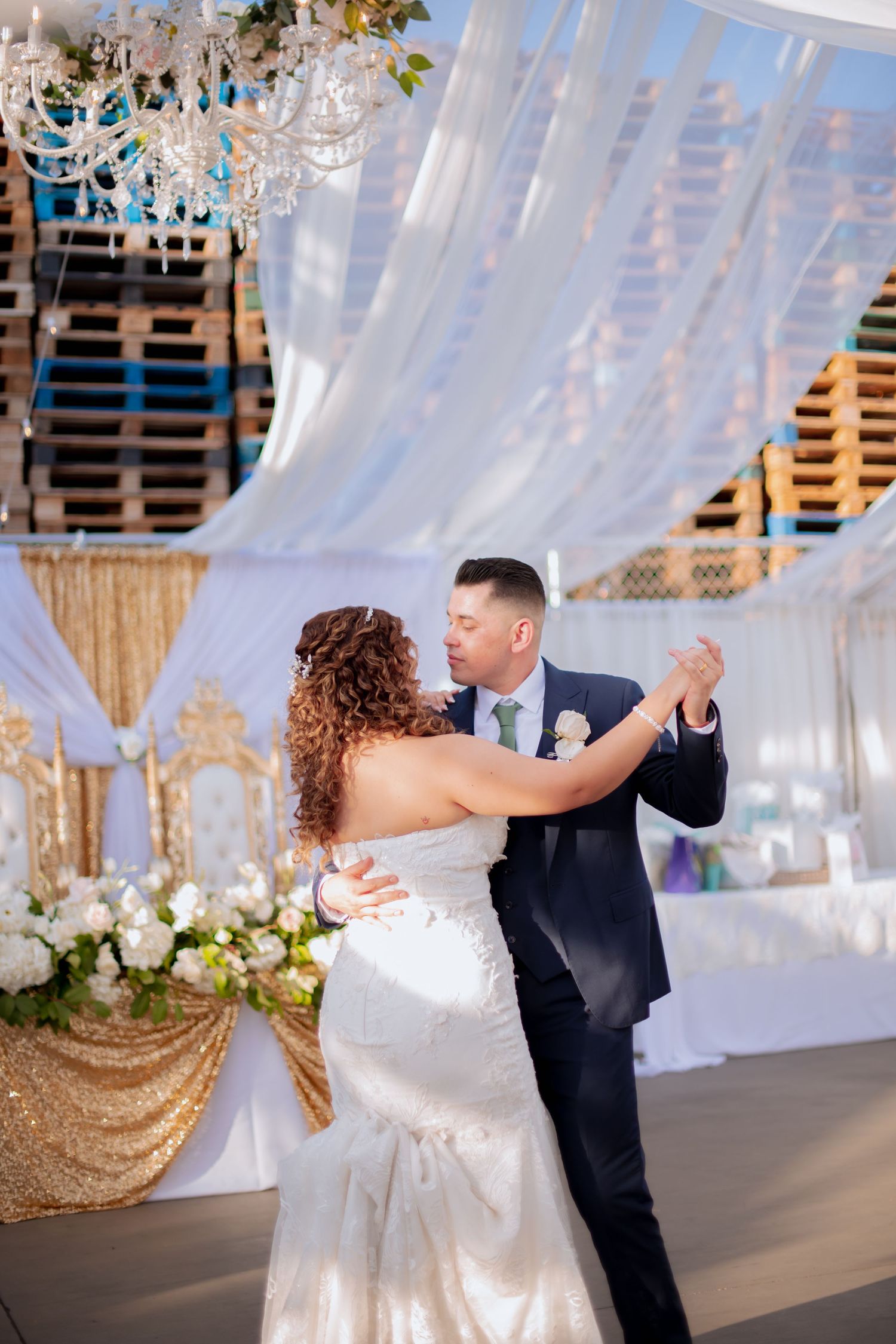 Couple performs an elegant dance move in a beautifully decorated wedding venue with white drapes and gold accents.