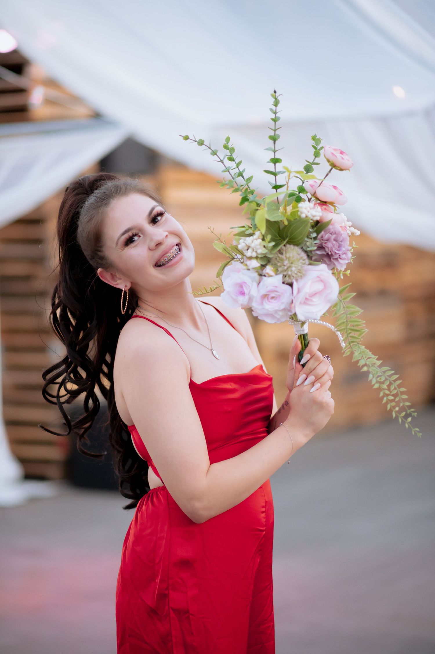 Woman in red formal dress holding delicate floral bouquet against white backdrop.