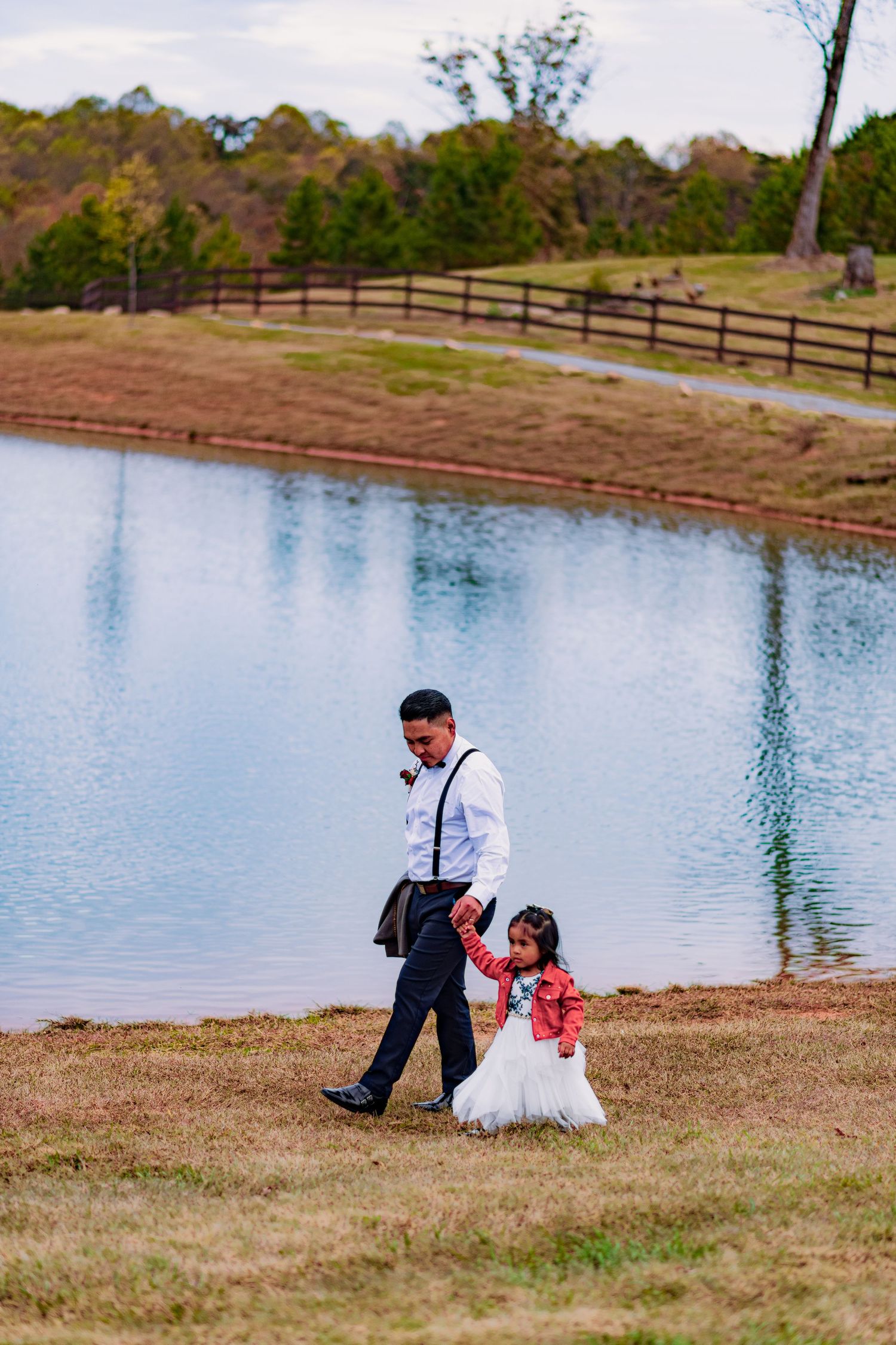 A scenic lakeside setting with rolling hills and wooden fencing in the background on a sunny day.