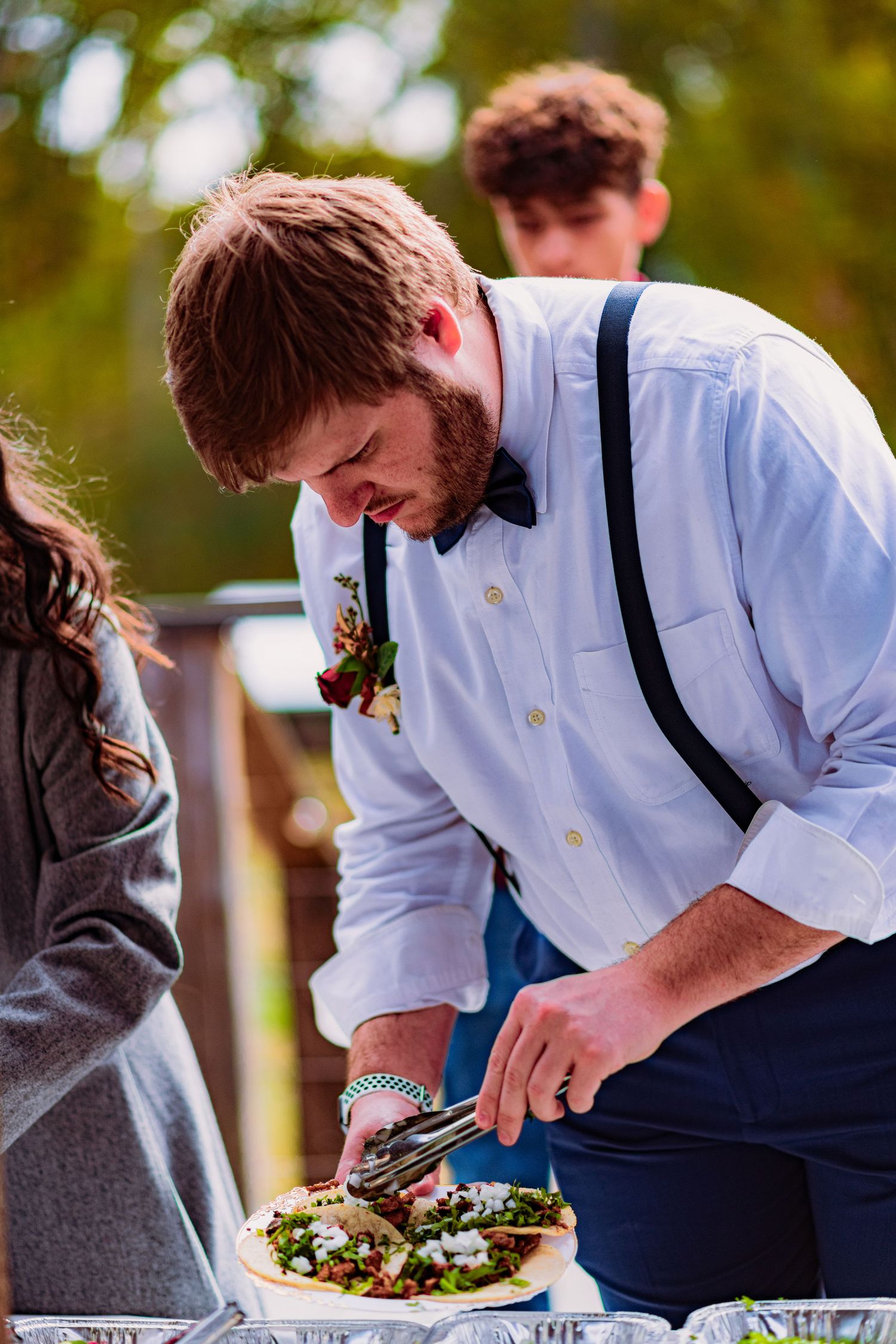 Person in white shirt and suspenders carefully plates food on a dish at an outdoor event.