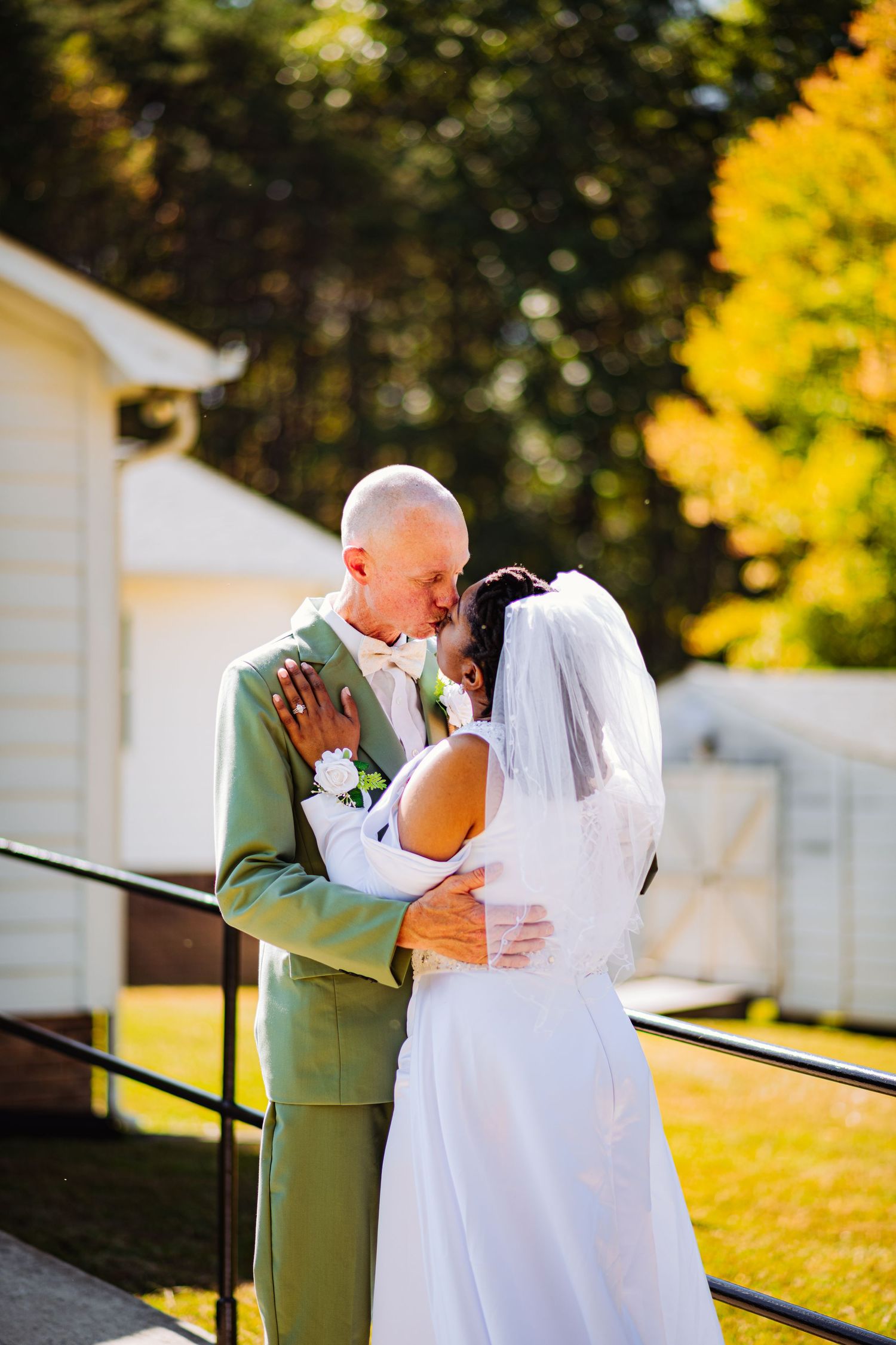 Newlyweds share tender moments in a garden setting with golden autumn foliage during sunset.