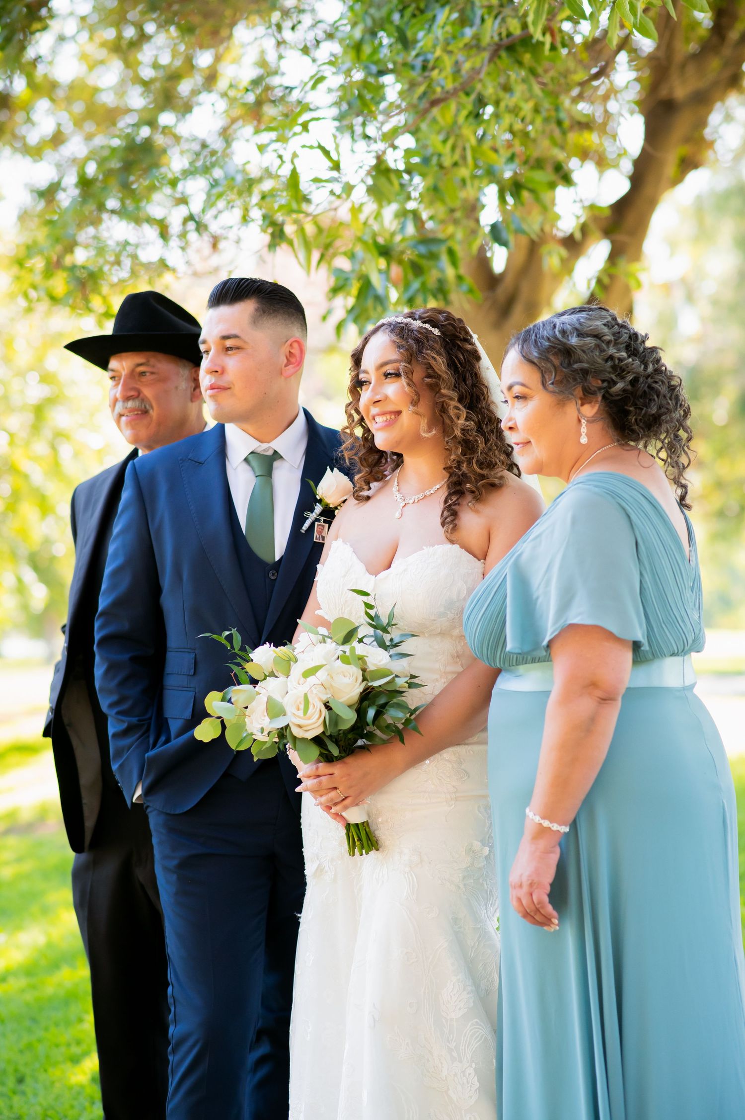 Wedding party in navy blue suits and mint green dresses poses together outdoors under trees.