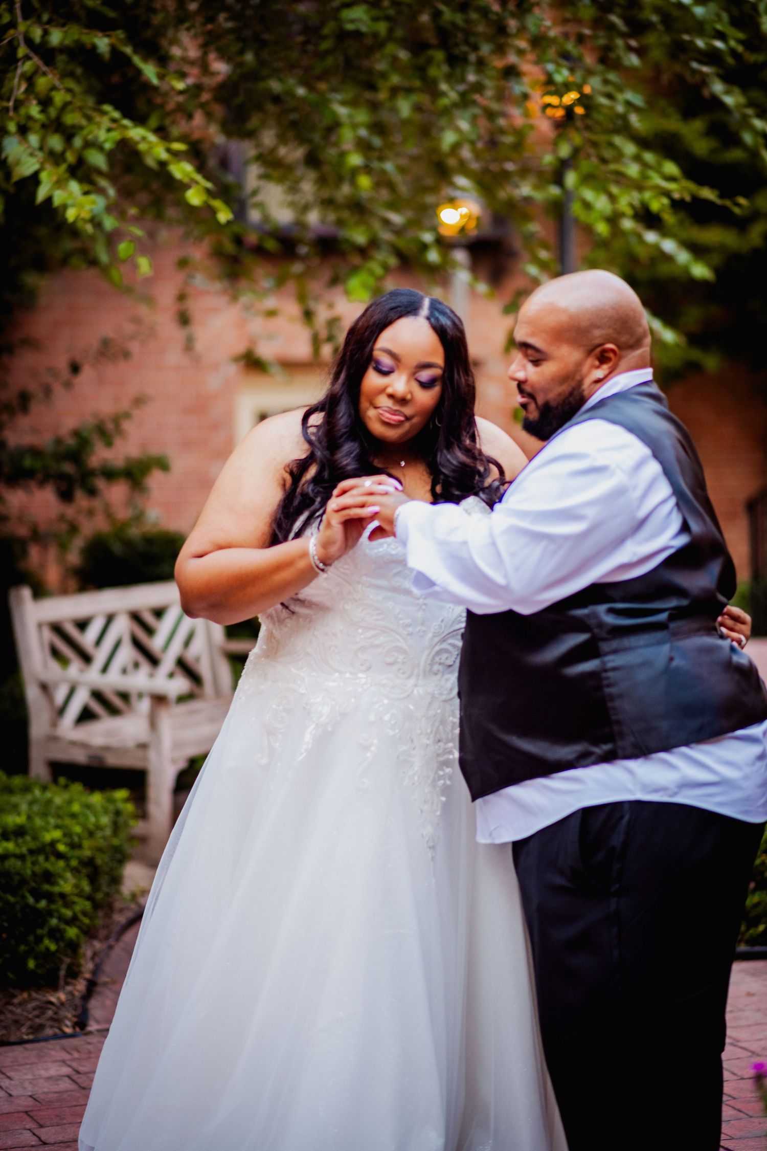 A couple shares a romantic dance moment outdoors in formal attire near a garden setting.