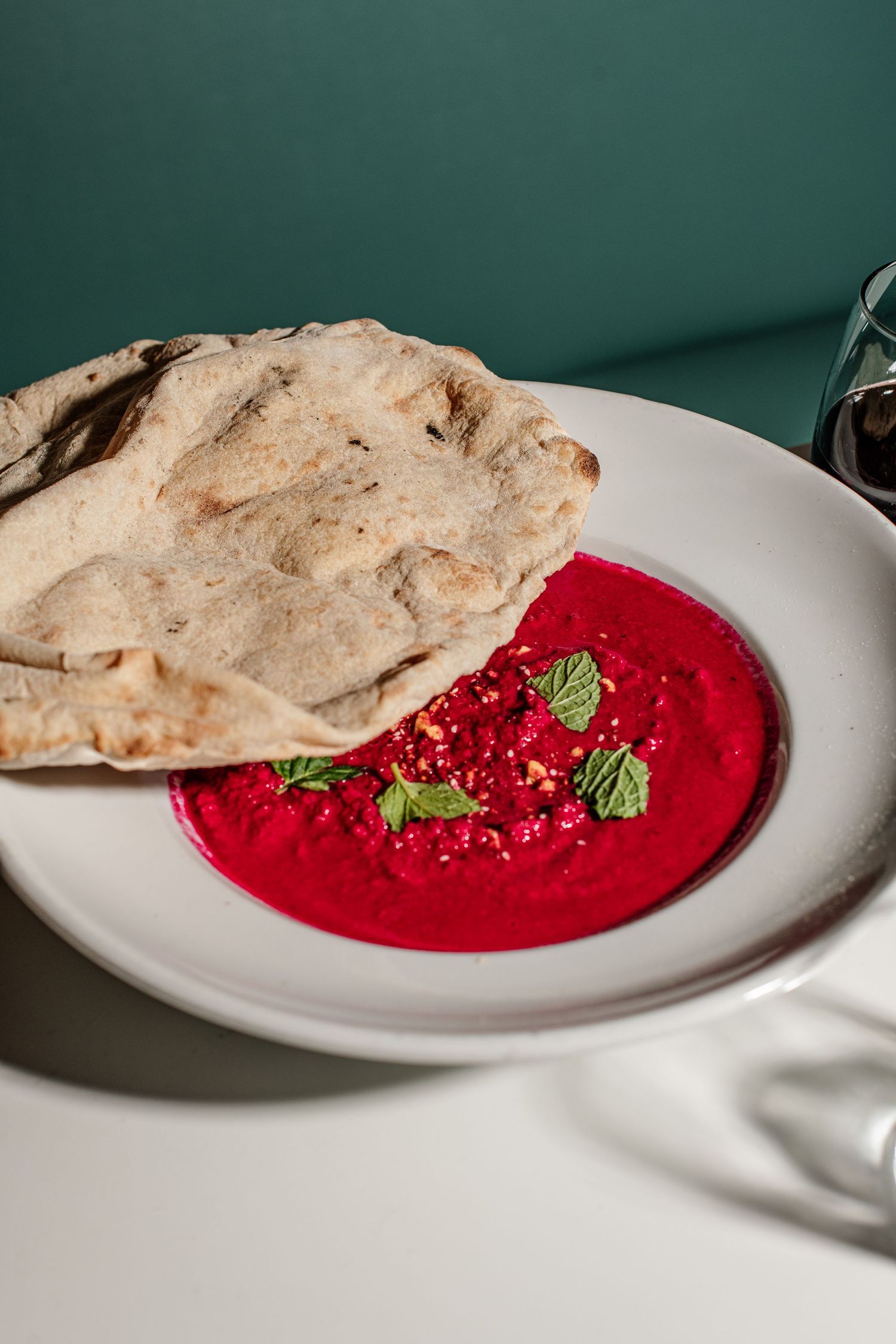Bright red beetroot hummus garnished with fresh mint leaves and spices, served with warm pita bread.