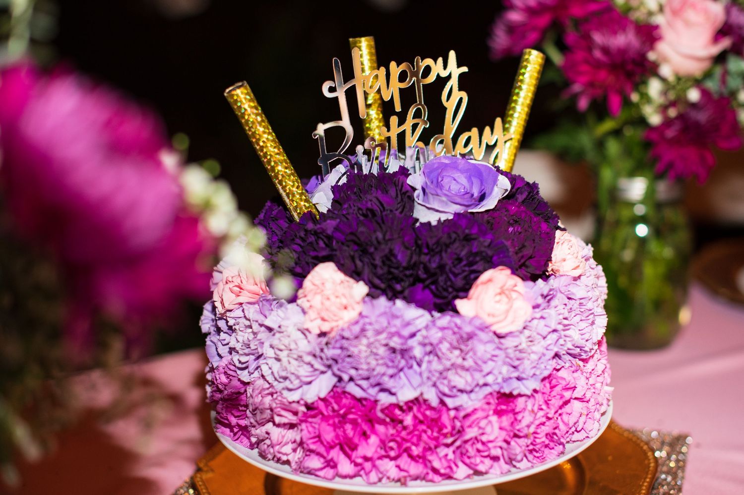 A decorative purple and pink floral cake topper with gold accents sits atop a festive celebration cake.