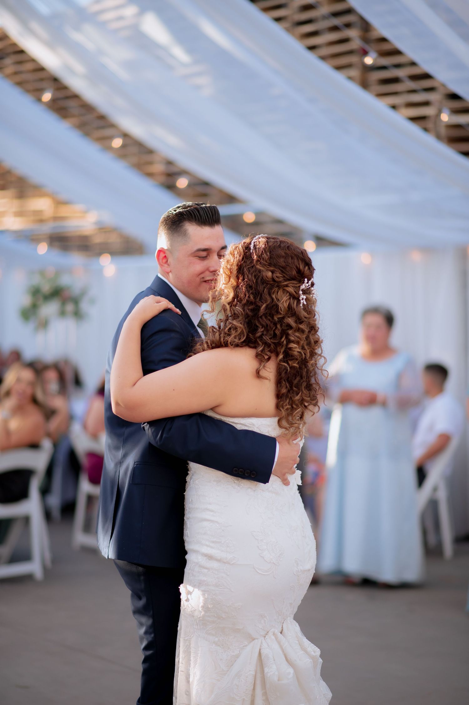 Couple dances together at their wedding reception under draped white fabric and twinkling lights.