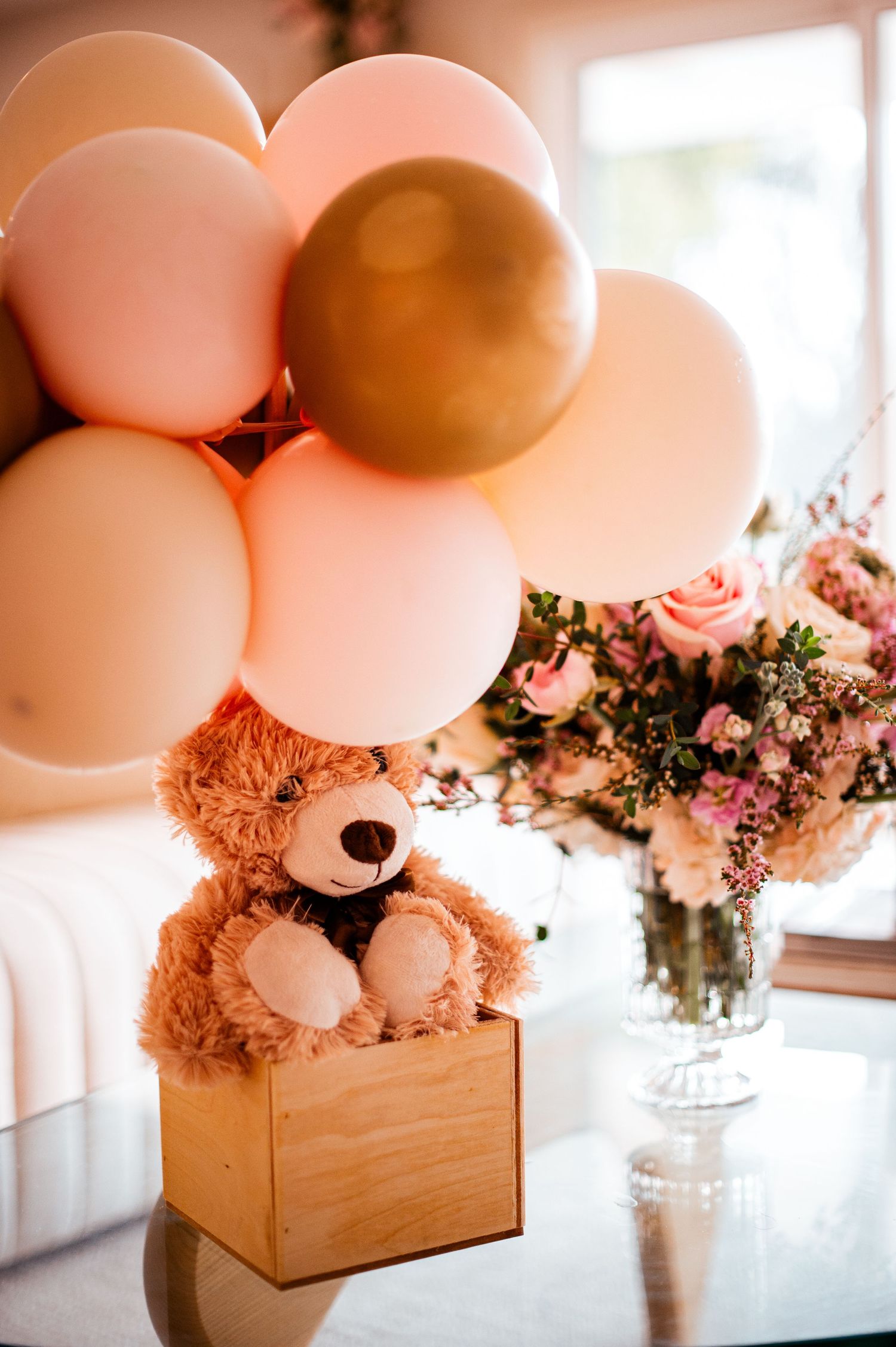 Decorative wooden box arrangement with pink balloons and flowers creating an elegant party centerpiece display.