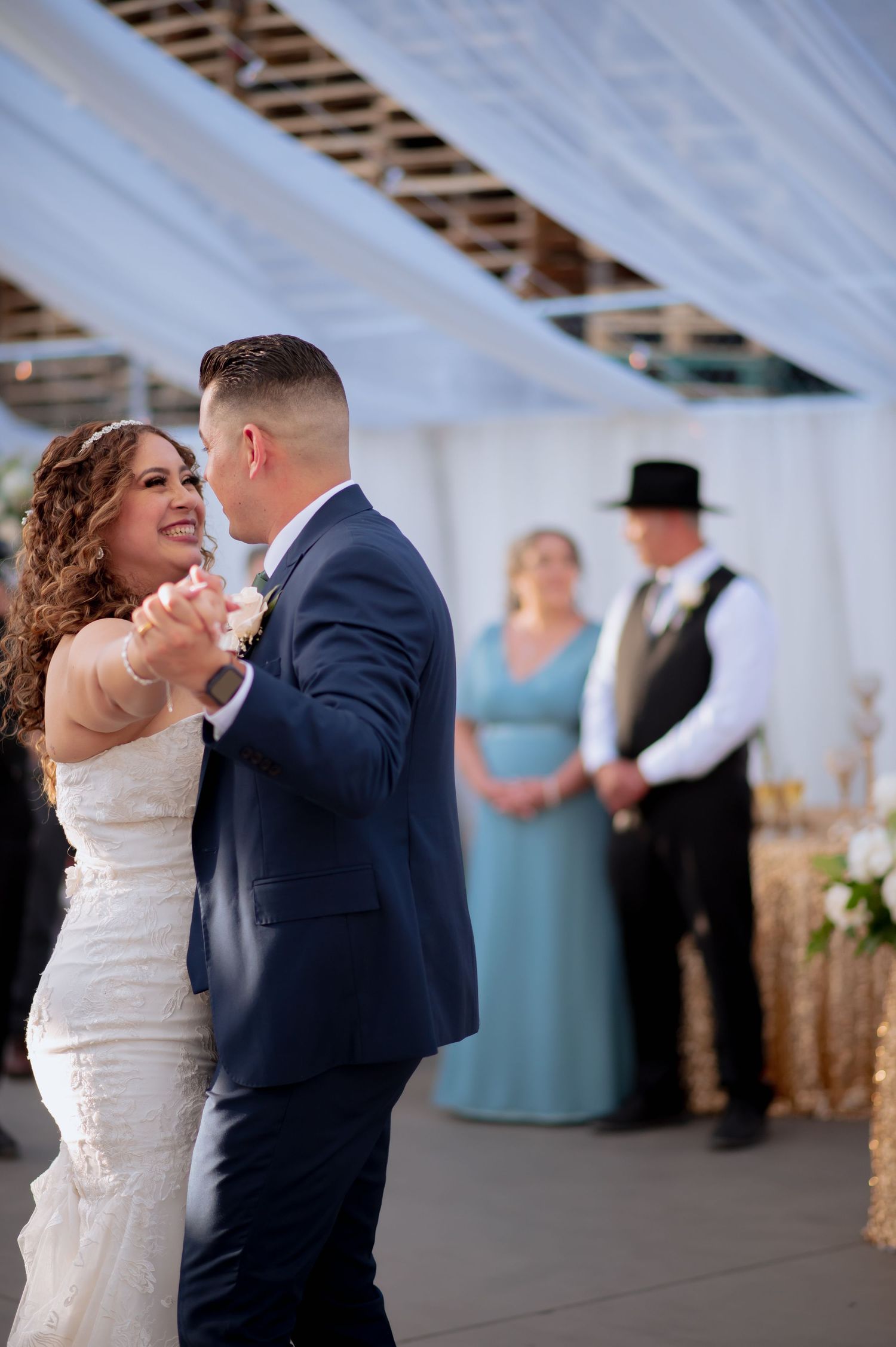 Newlyweds share intimate dance moves at their reception with gold decor and white draping.