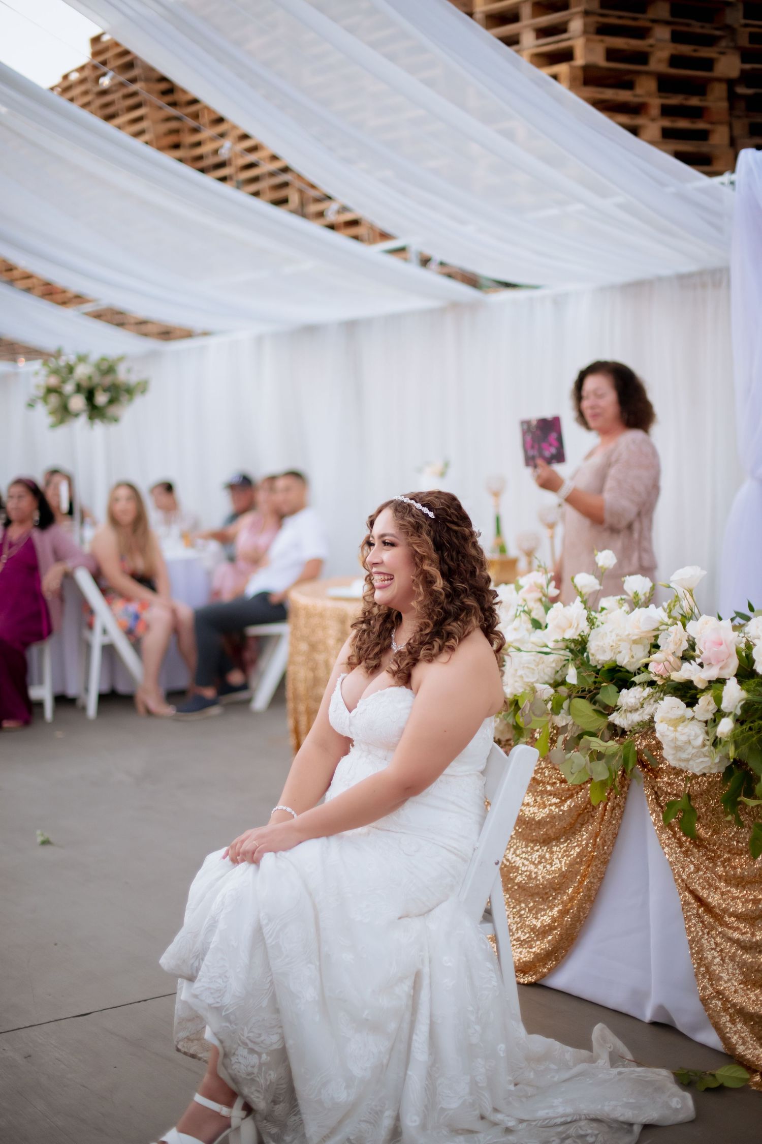 A dreamy wedding reception in a white draped tent with gold sequined chairs and floral arrangements.