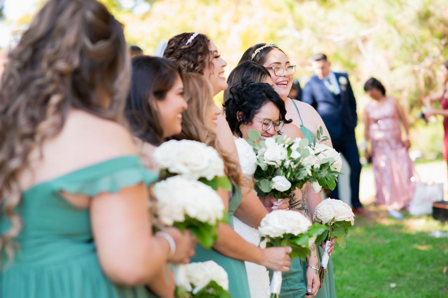 Wedding party members share joyful moments together under trees.