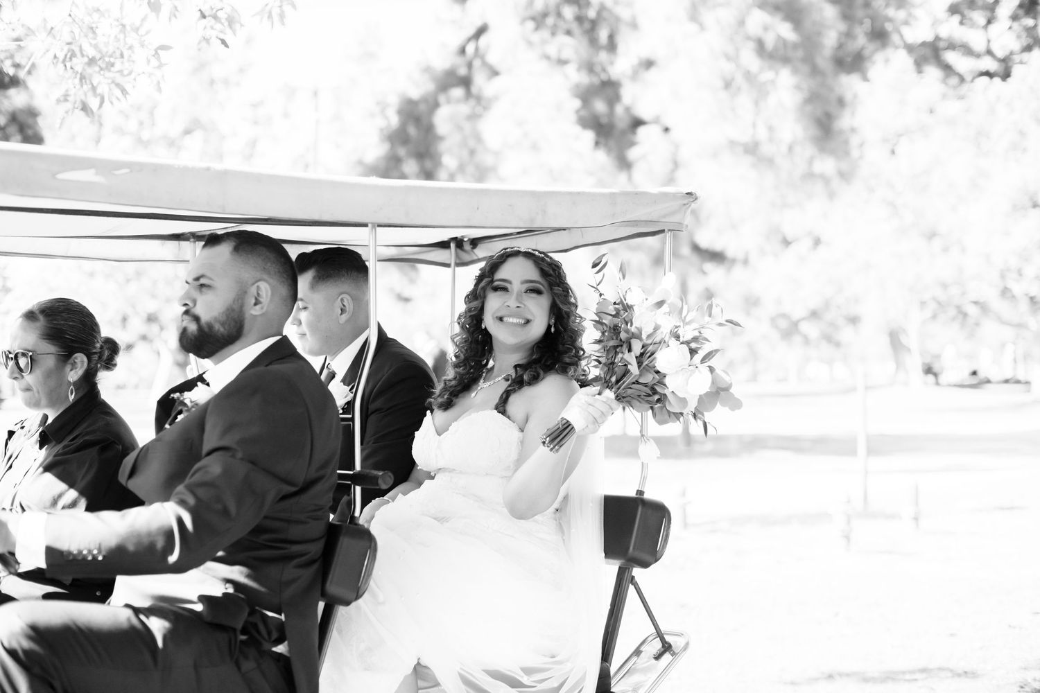 Black and white photo of wedding couple riding in golf cart .