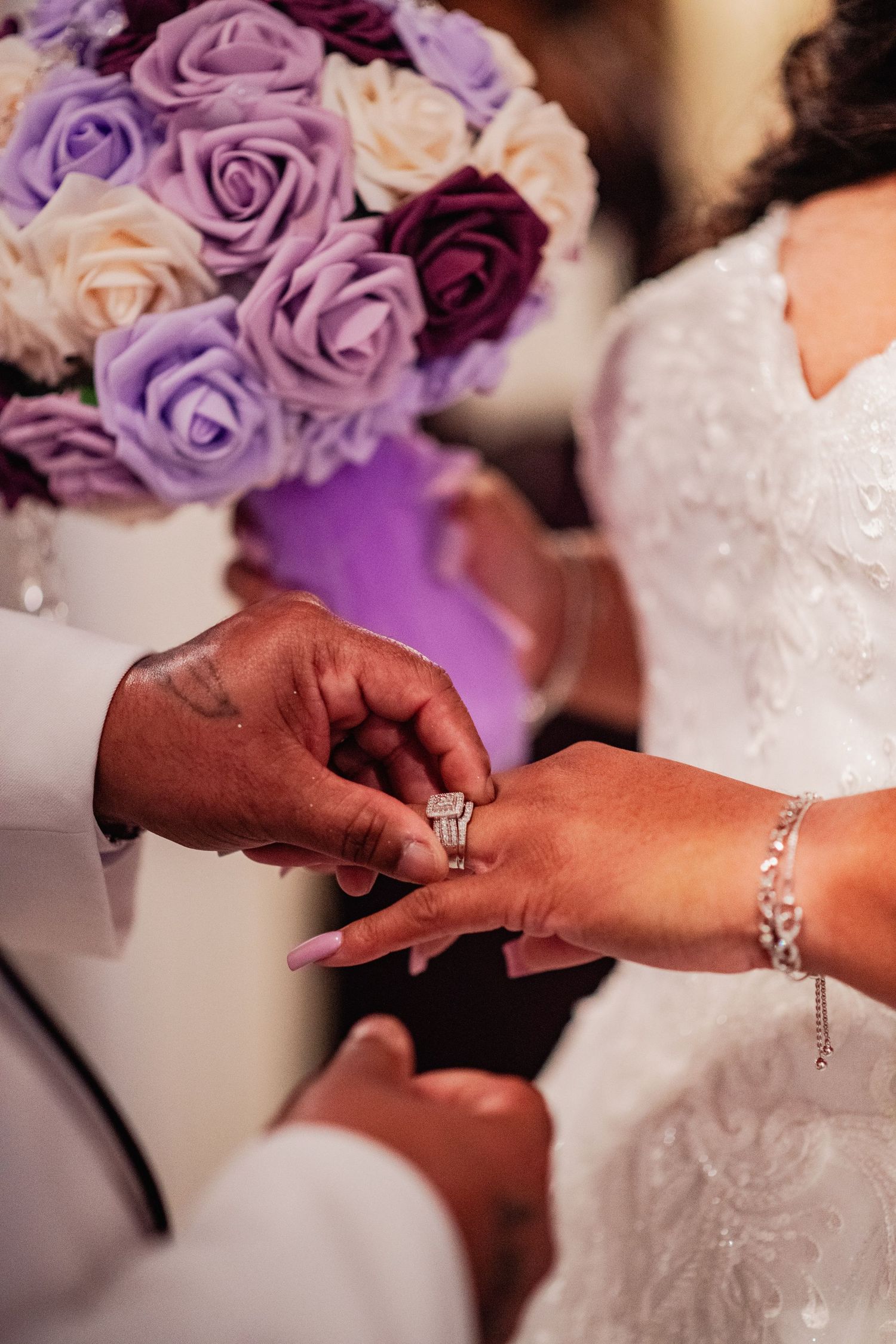 Close-up sequence showing hands exchanging wedding rings during a ceremony with purple roses in background.