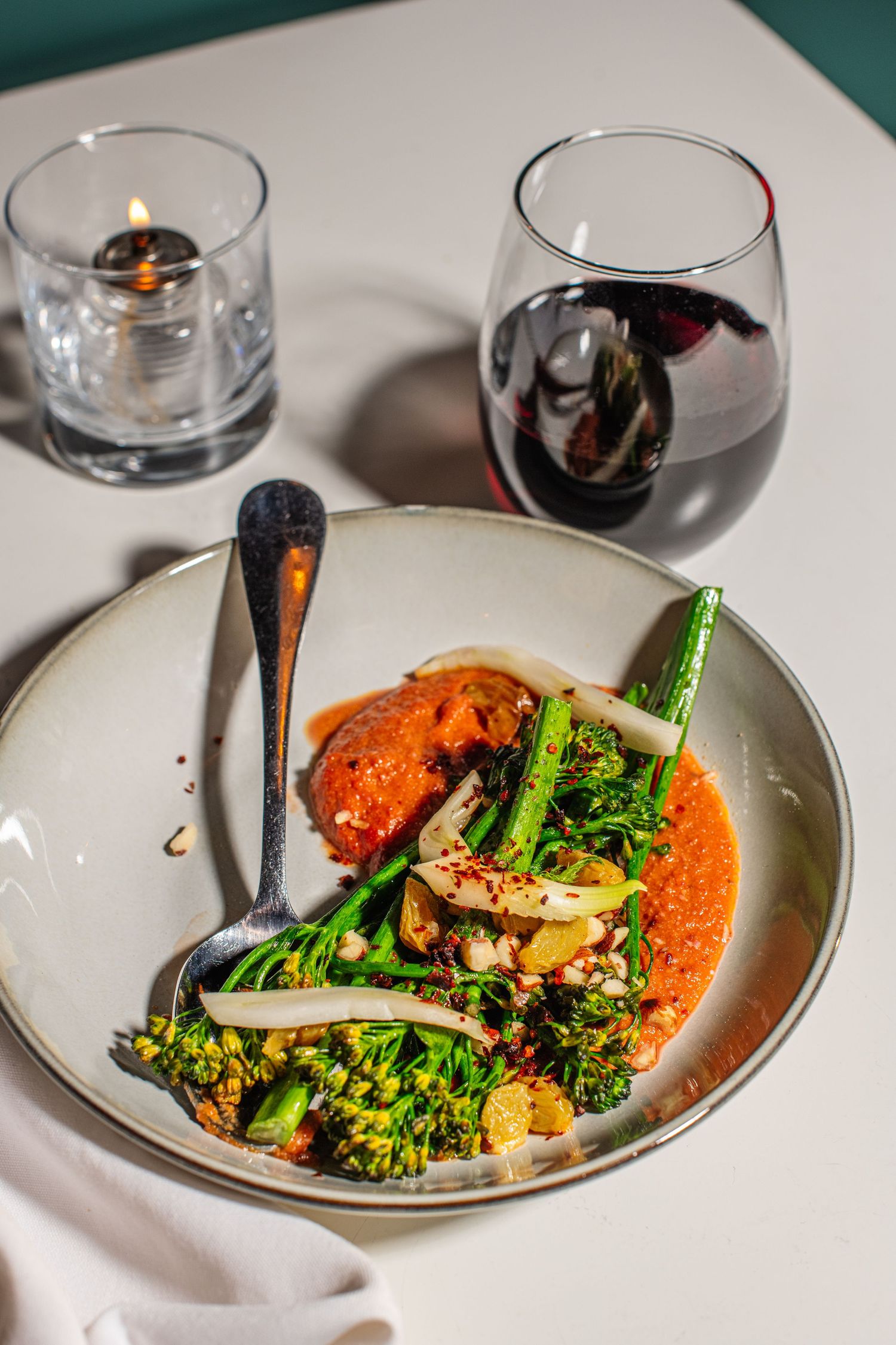 Elegant plating of roasted vegetables with bright orange sauce and fresh herbs served alongside a glass of red wine.